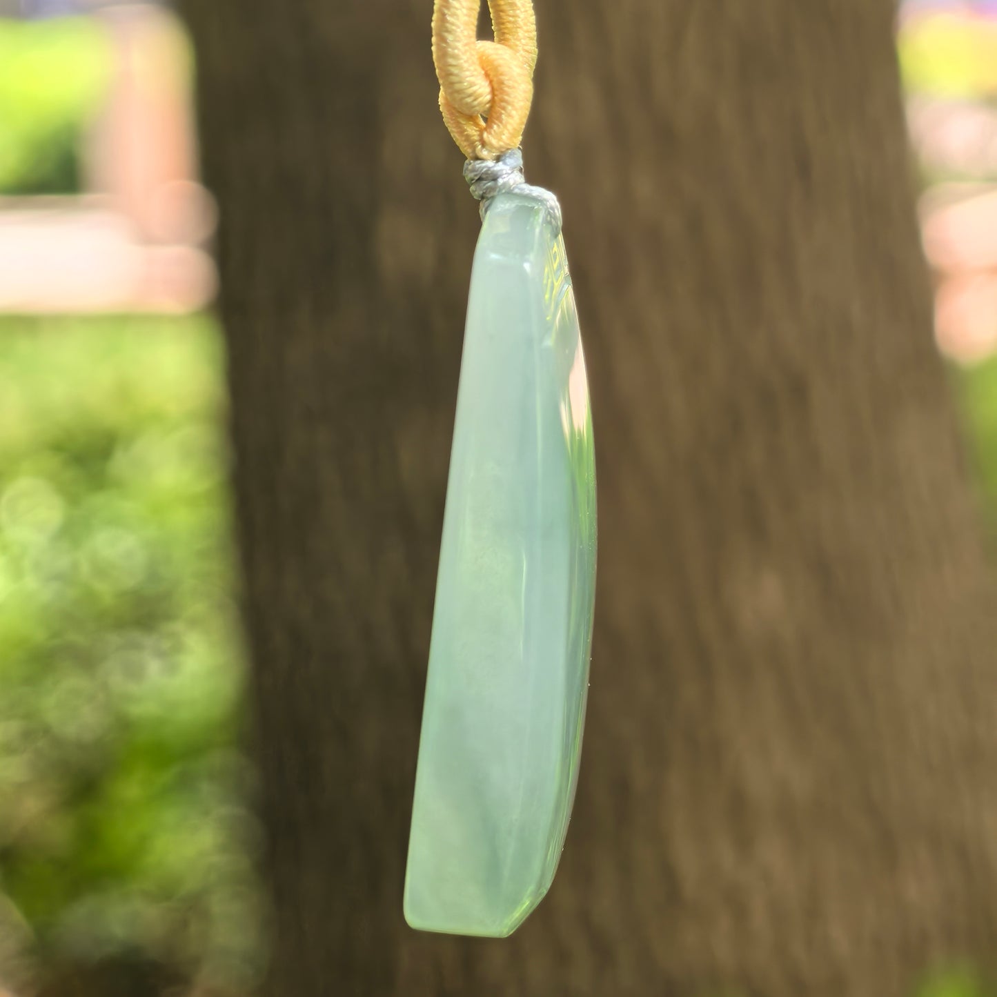 Side view of lake green plain jade plaque pendant showing its curved front surface and thickness.