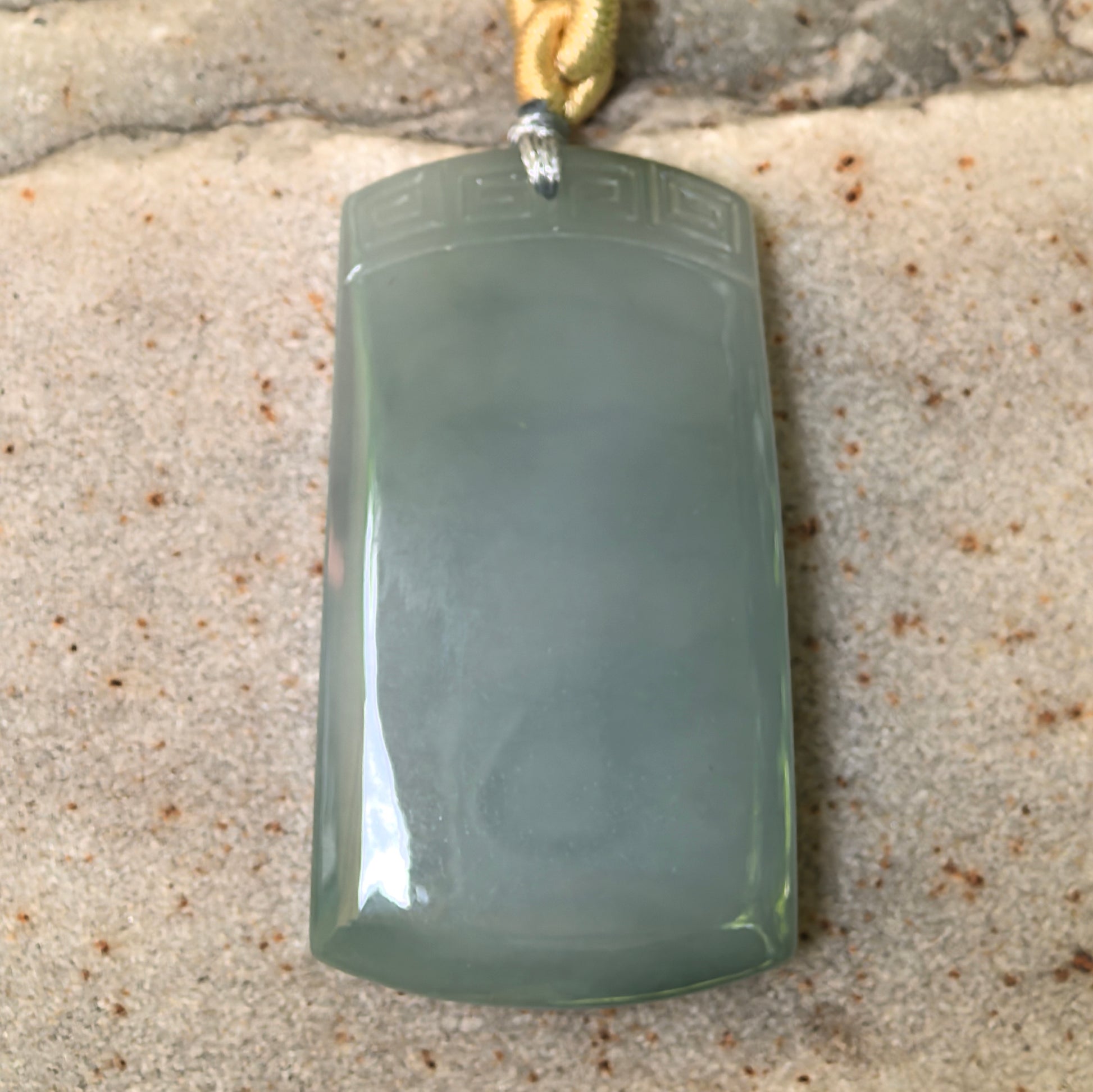 Close-up of fine glutinous lake green plain jade plaque pendant on stone background with antique-style top pattern.
