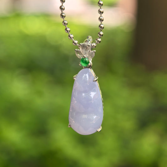 Natural Grade-A icy glutinous violet bean jadeite pendant with 18K gold setting hanging against green outdoor background.