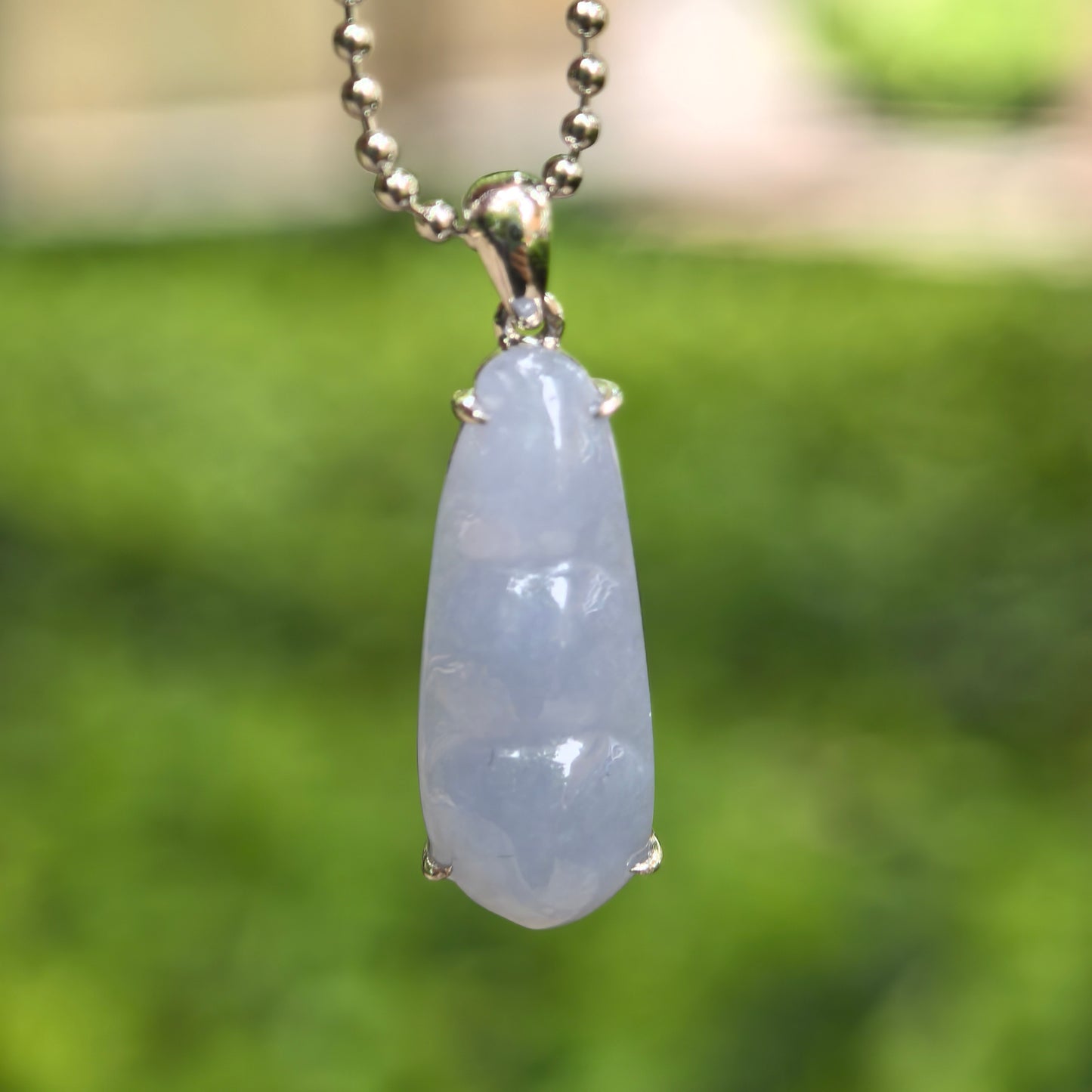 Natural Grade-A icy glutinous violet bean jadeite pendant with 18K gold setting hanging against green outdoor background.