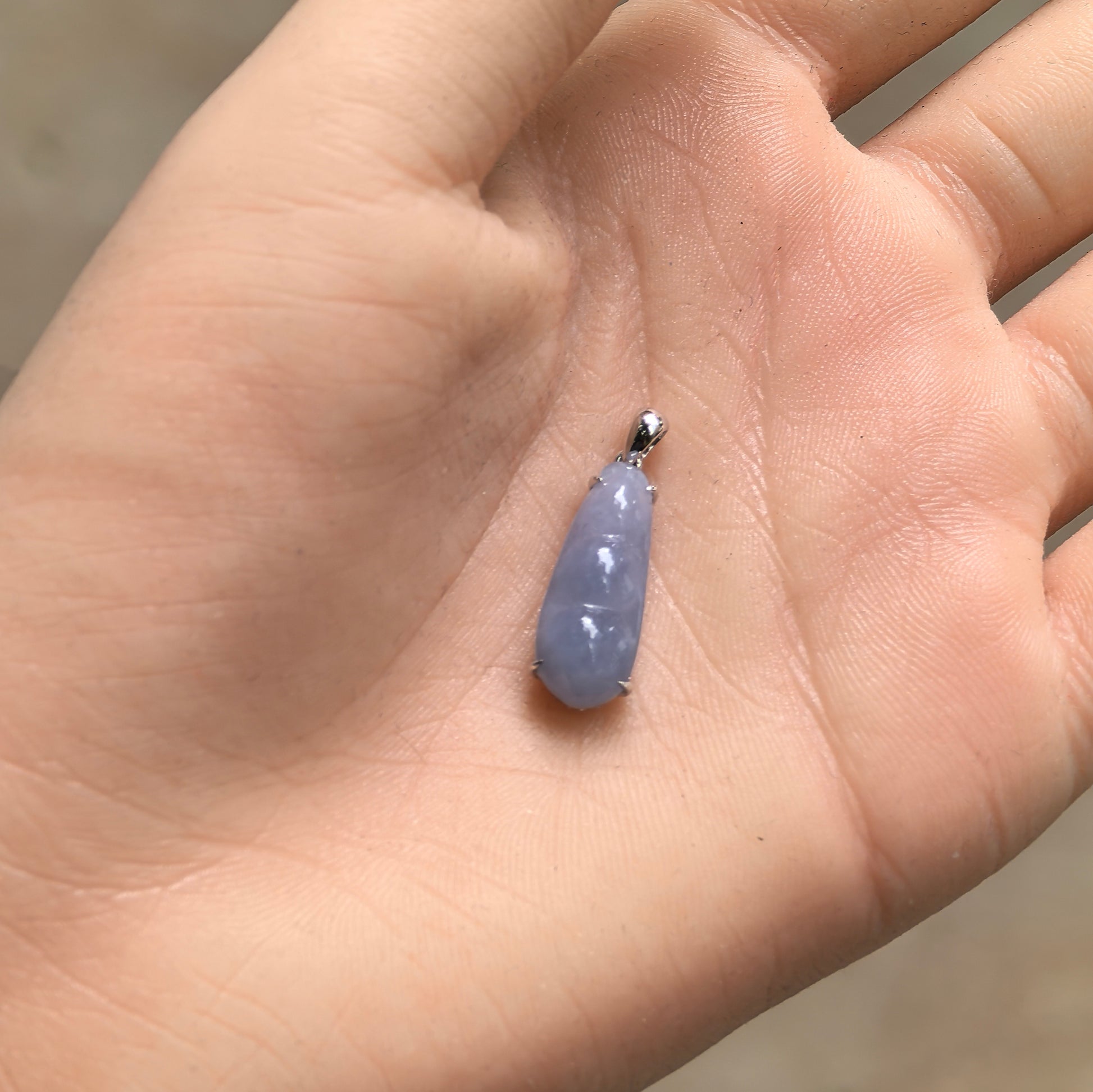 Handheld icy glutinous violet bean jadeite pendant showing small size, soft violet tone, and polished surface.