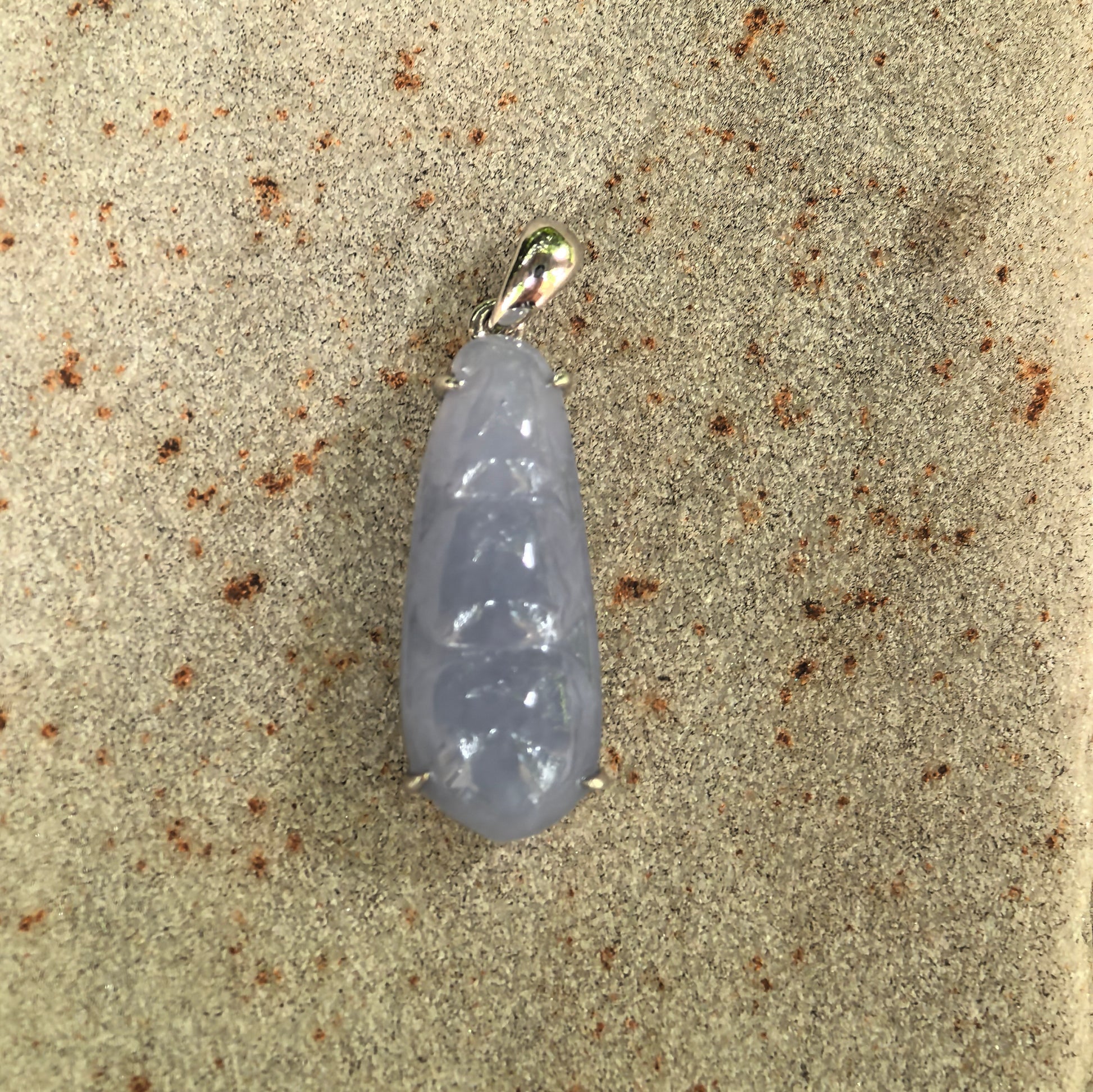 Close-up of violet bean jadeite pendant on stone background showing raised bean carving and white-metal 18K gold setting.