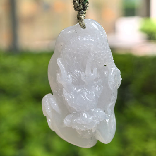 Natural Grade-A glutinous pale lavender-white dragon jadeite pendant hanging on cord with outdoor green background.