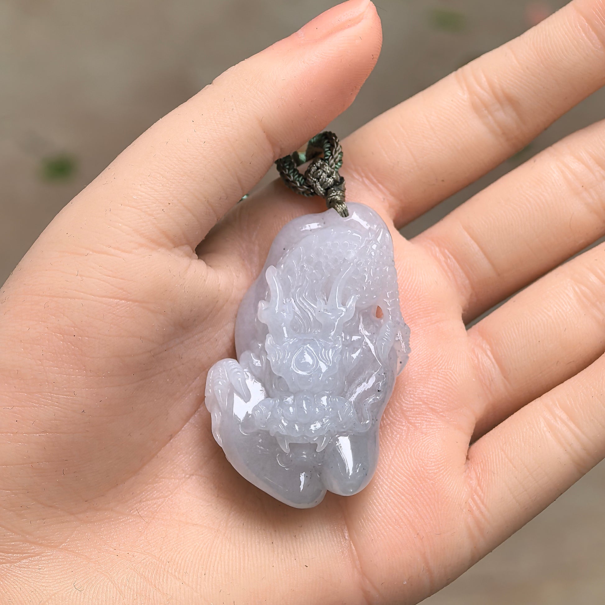 Handheld Natural Grade-A dragon jadeite pendant showing compact size, raised carving, and pale lavender-white tone.

