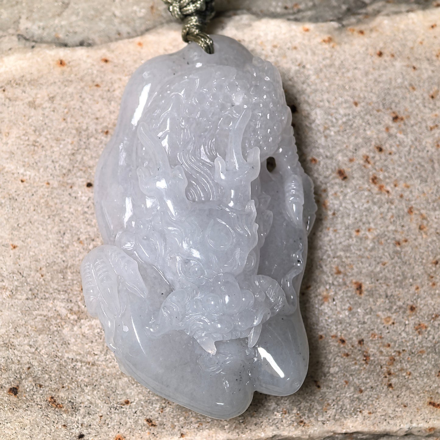 Close-up of three-dimensional glutinous dragon jadeite pendant on stone background with sculptural carving details.
