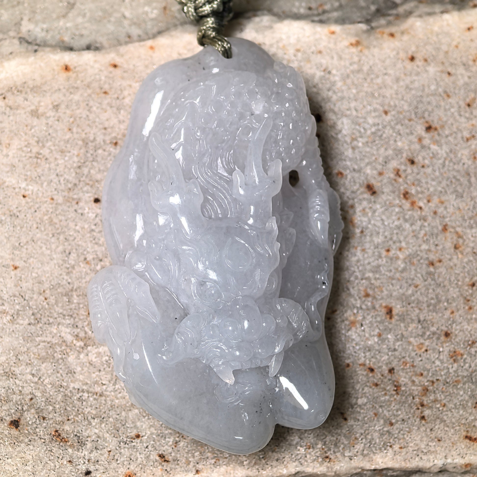 Close-up of three-dimensional glutinous dragon jadeite pendant on stone background with sculptural carving details.
