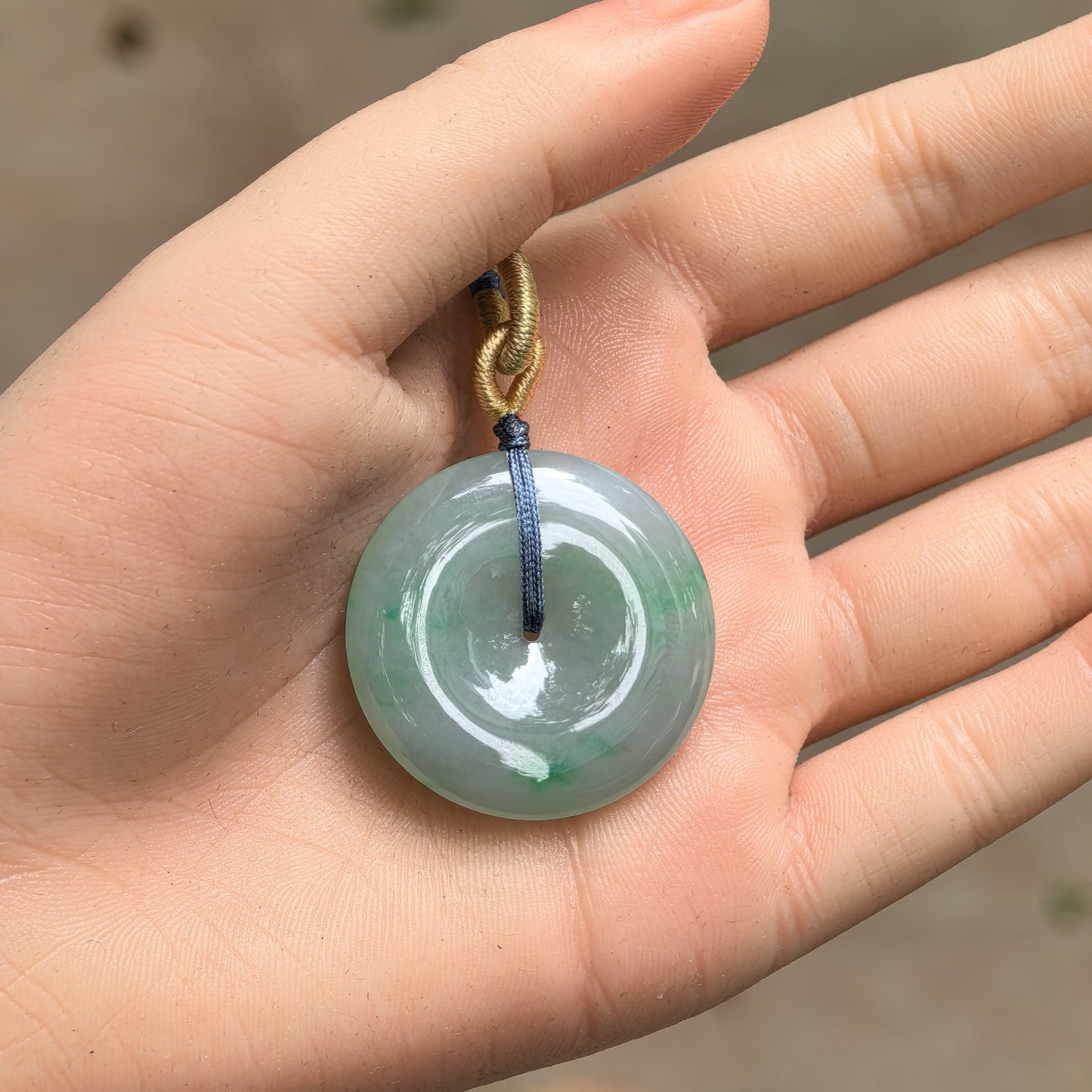 Handheld large green jadeite Peace Pendant showing round disc shape, central opening, and smooth curved surface.