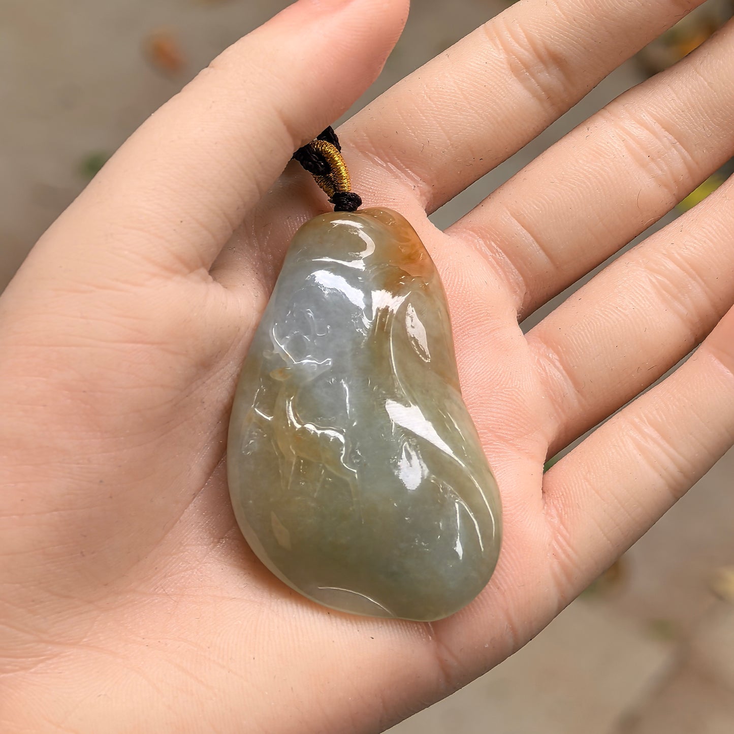 Natural Grade-A glutinous yellow-green deer jadeite pendant shown in hand with warm natural color variation.
