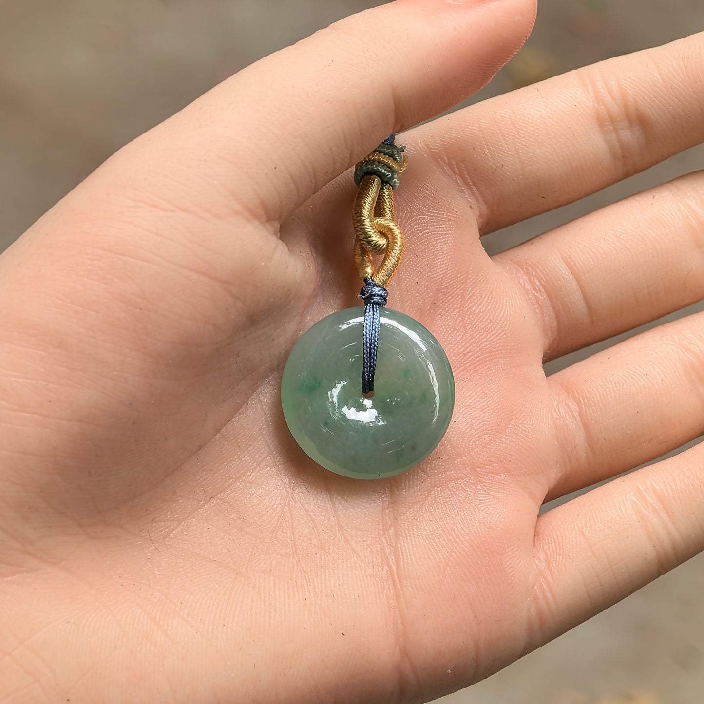 Handheld glutinous green jadeite Peace Pendant showing compact size, smooth round shape, and central opening.