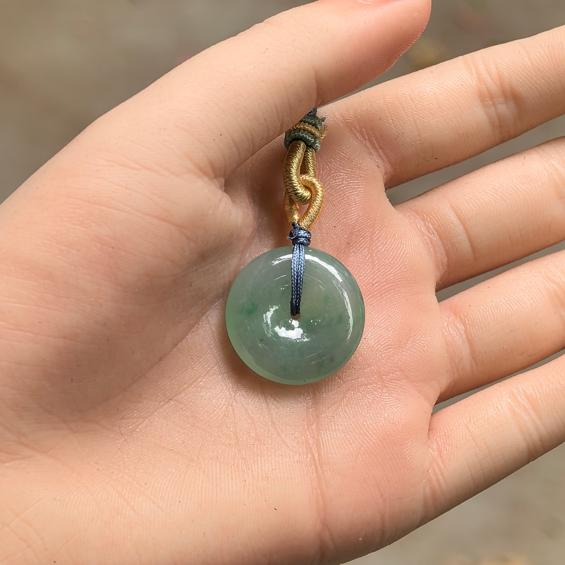 Handheld glutinous green jadeite Peace Pendant showing compact size, smooth round shape, and central opening.