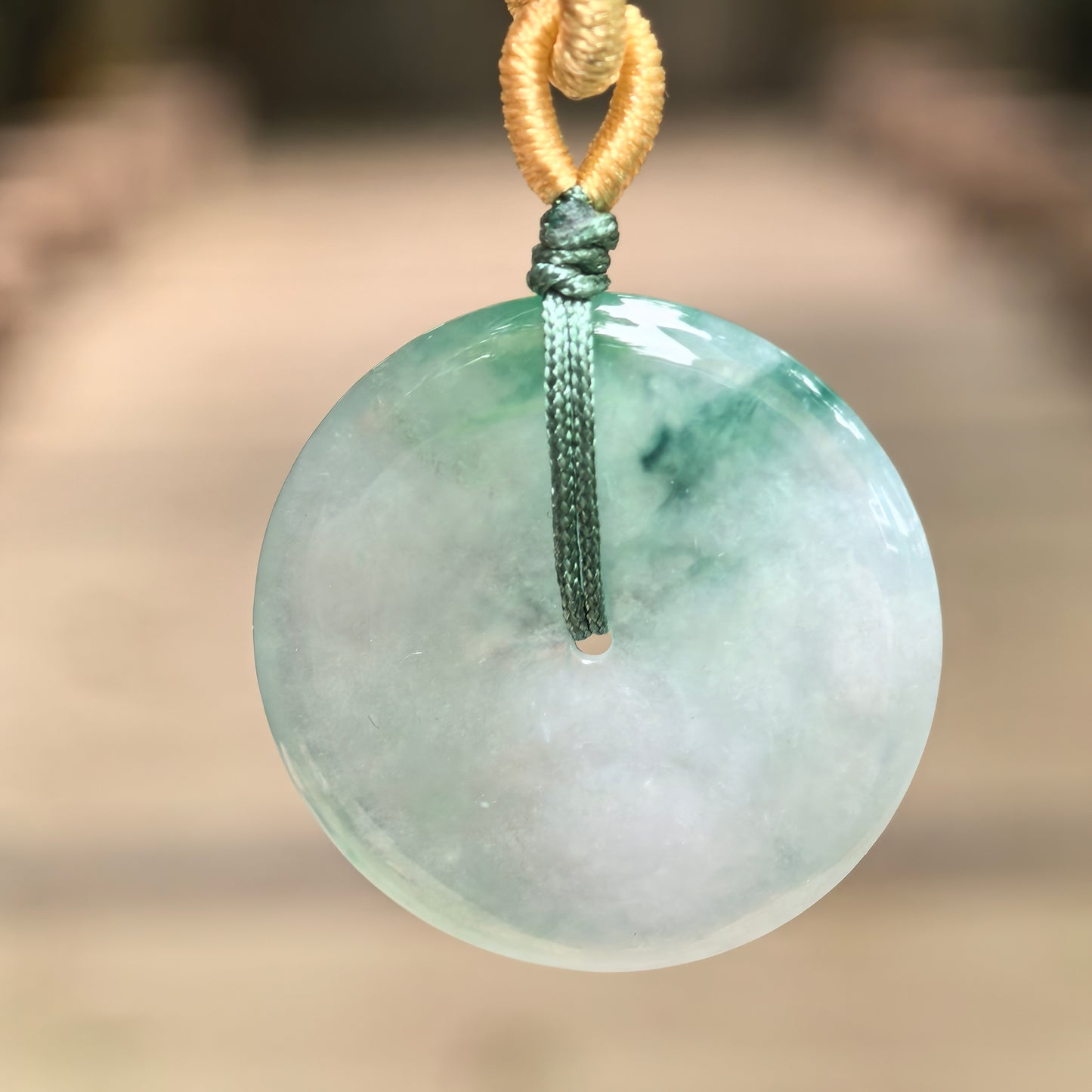 Close-up of floating green Peace Buckle jadeite pendant showing round disc shape and gel-like luster.
