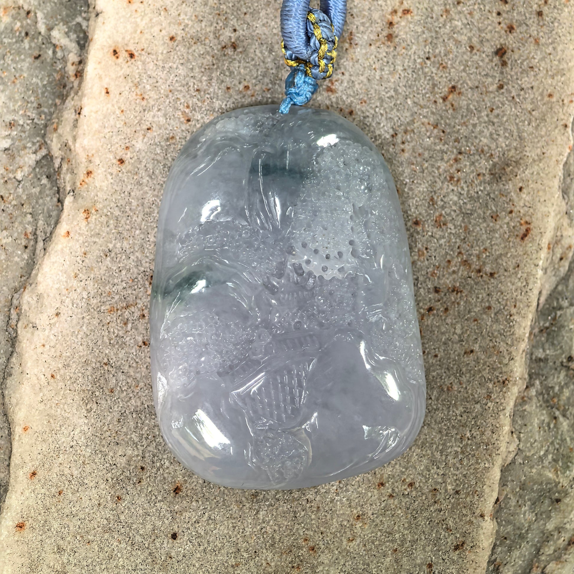 Close-up of glutinous lavender landscape jadeite pendant placed on stone, showing detailed mountain-and-water carving.
