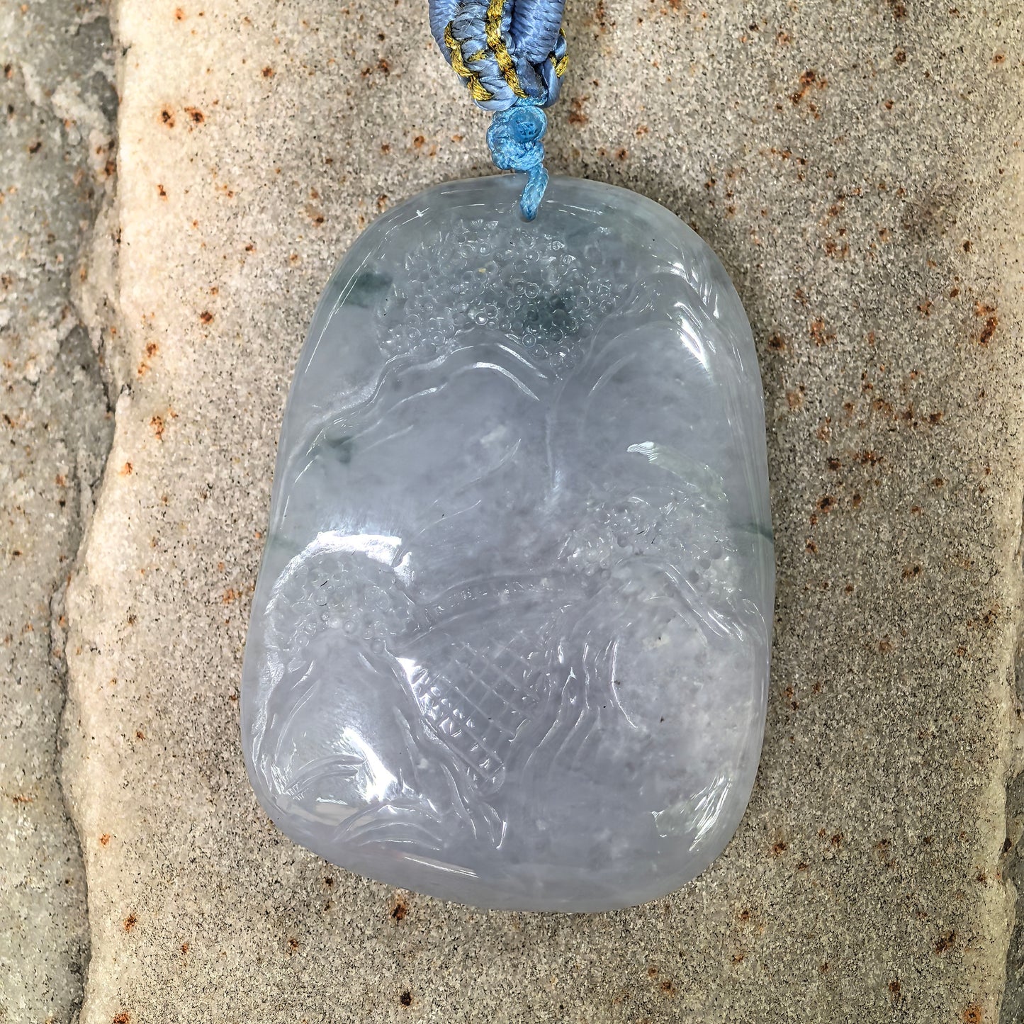 Back view of natural lavender landscape jadeite pendant with pale green accents on stone background.
