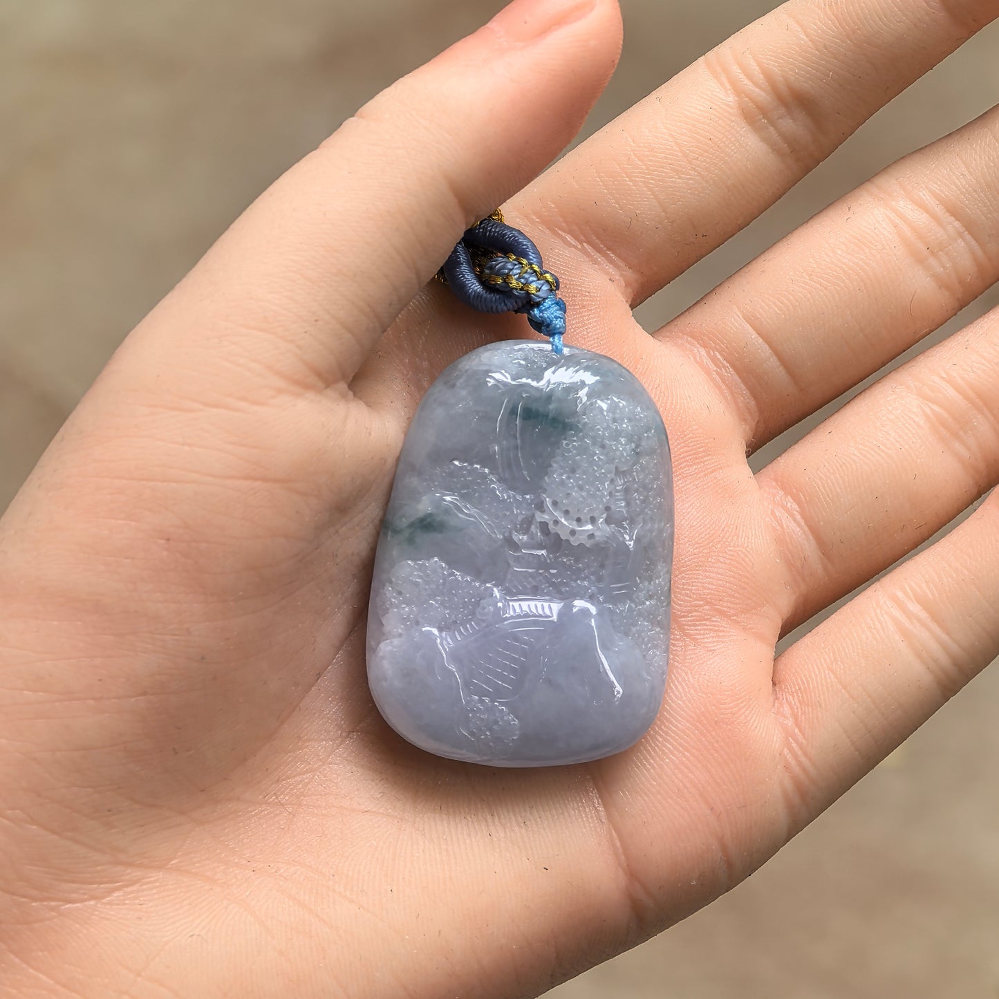 Hand-held view of natural Grade-A lavender landscape jadeite pendant with cord for size reference.
