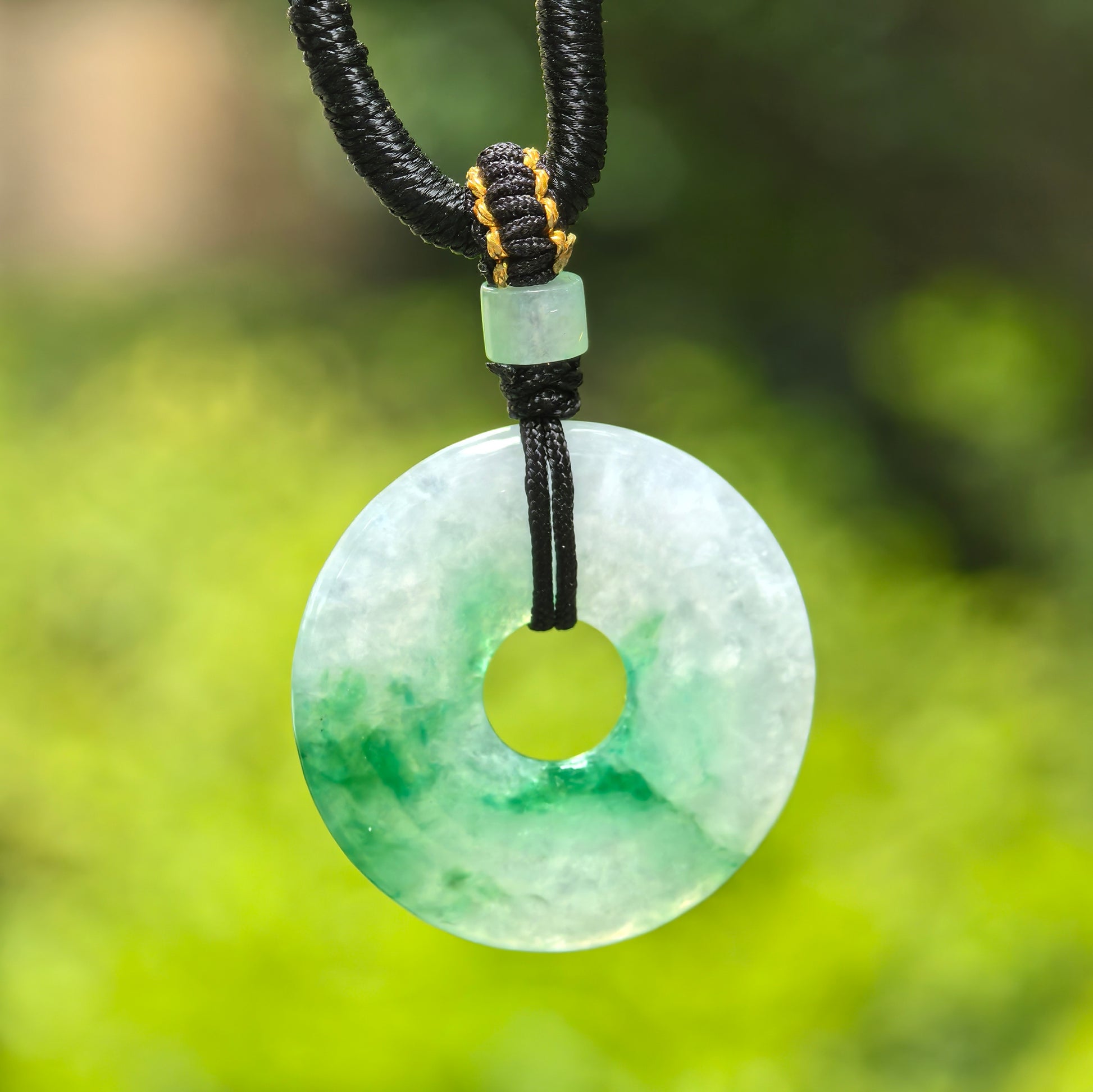 Close-up of white-based green jadeite donut pendant showing round ring shape, central opening, and vivid green color.
