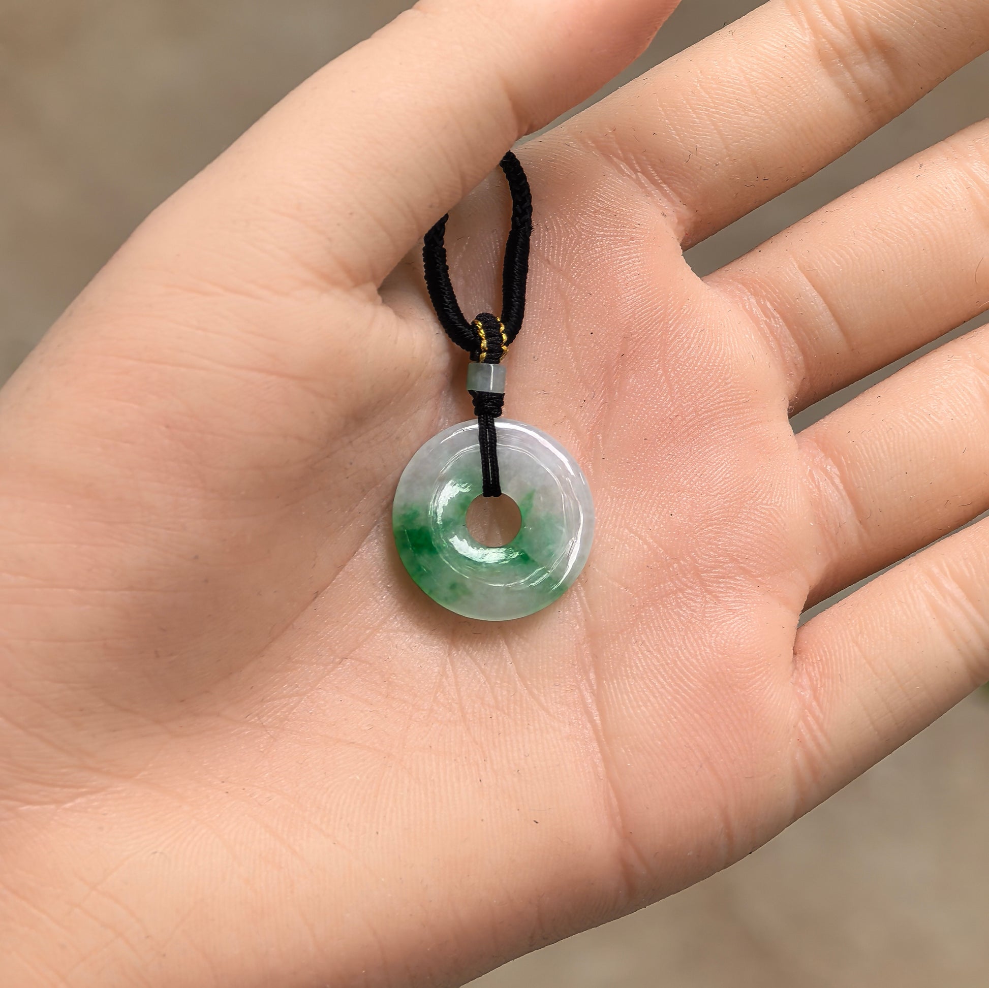 Handheld Natural Grade-A green and light green donut jadeite pendant showing petite size and polished surface.
