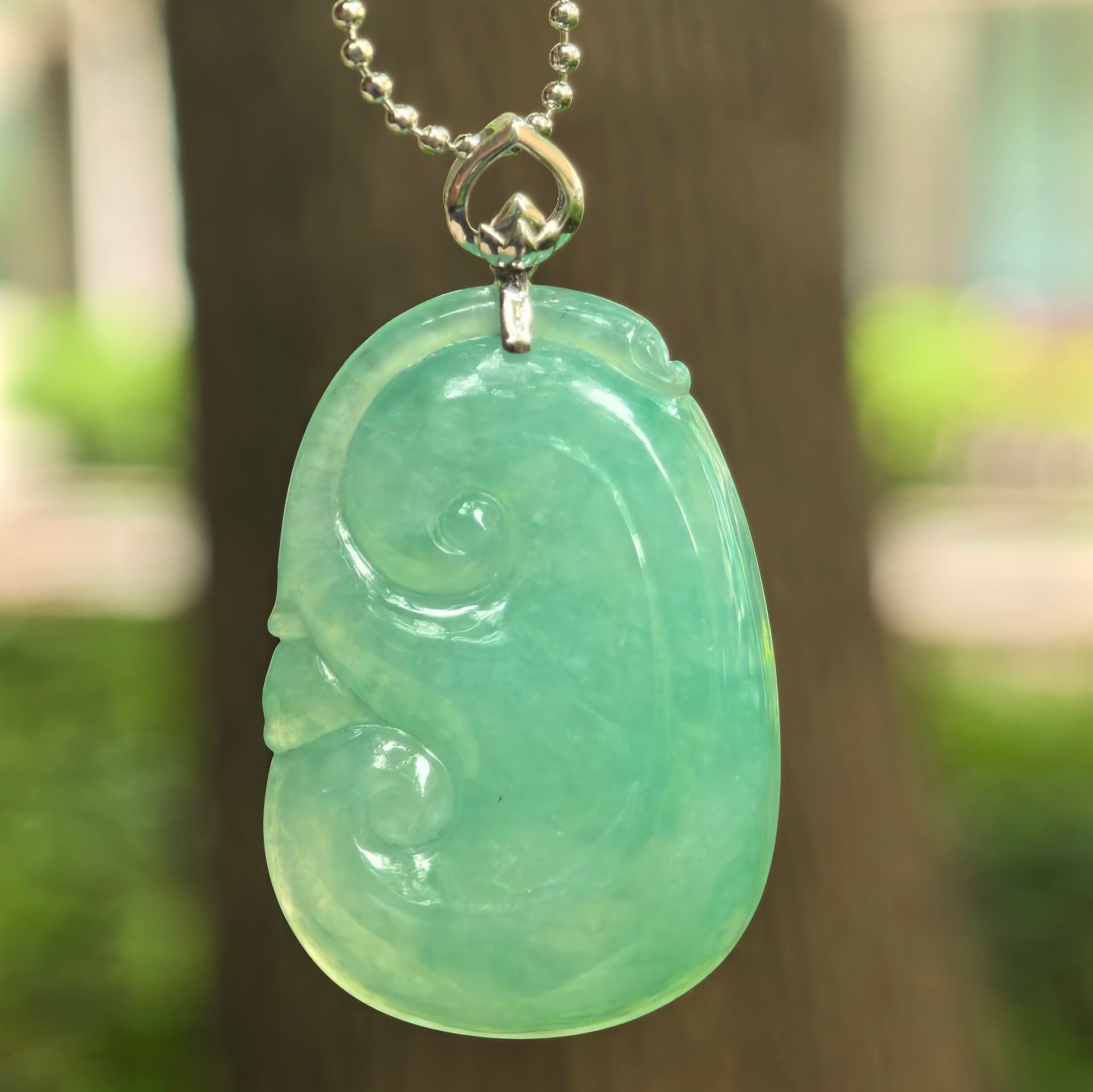 Natural Grade-A icy glutinous fruit green Ruyi jadeite pendant with 18K gold setting hanging outdoors.