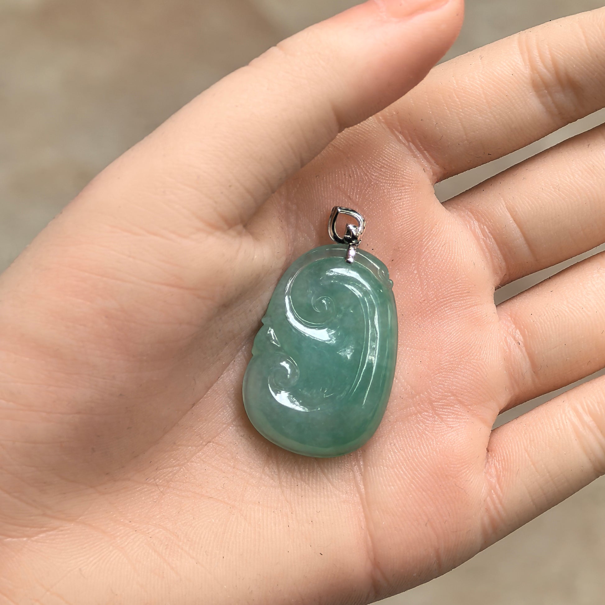 Handheld Natural Grade-A fruit green Ruyi jadeite pendant with 18K gold setting and rounded shape.