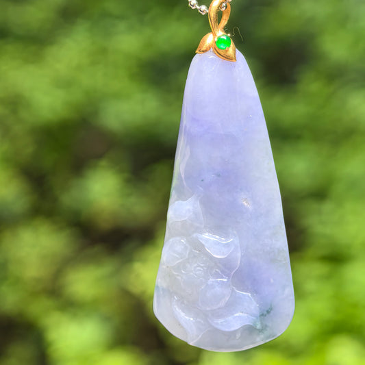 Natural Grade-A icy glutinous blue-lavender lotus jadeite pendant with 18K gold setting against green outdoor background.
