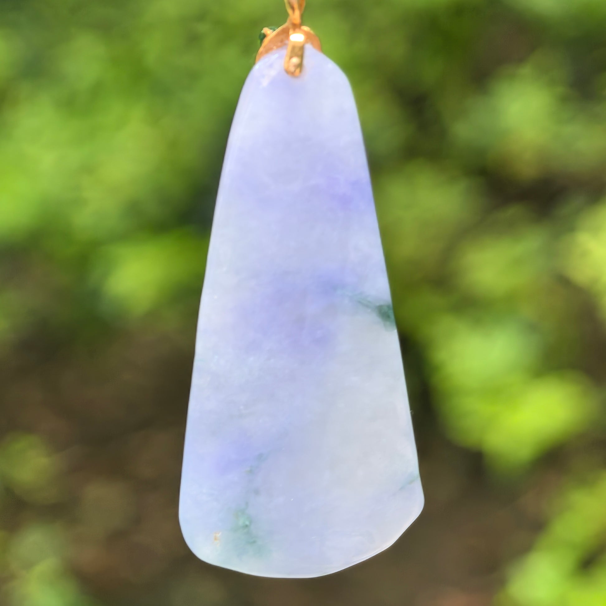 Back view of blue-lavender jadeite pendant showing soft translucency, natural green accents, and tapered shape.
