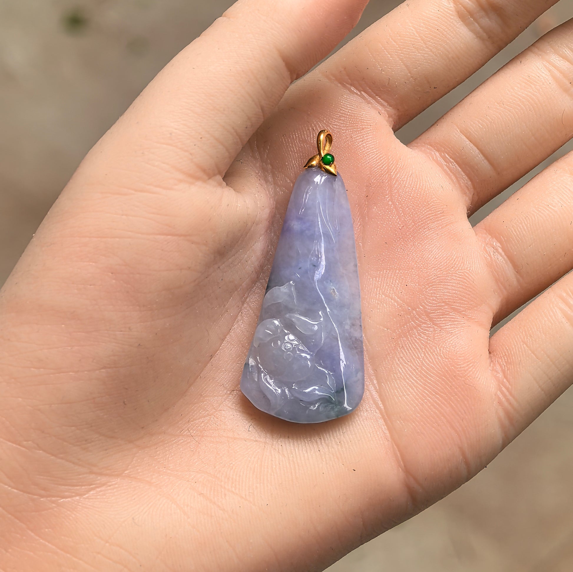 Handheld 18K gold lotus jadeite pendant showing blue-lavender color, small green accent stone, and compact size.
