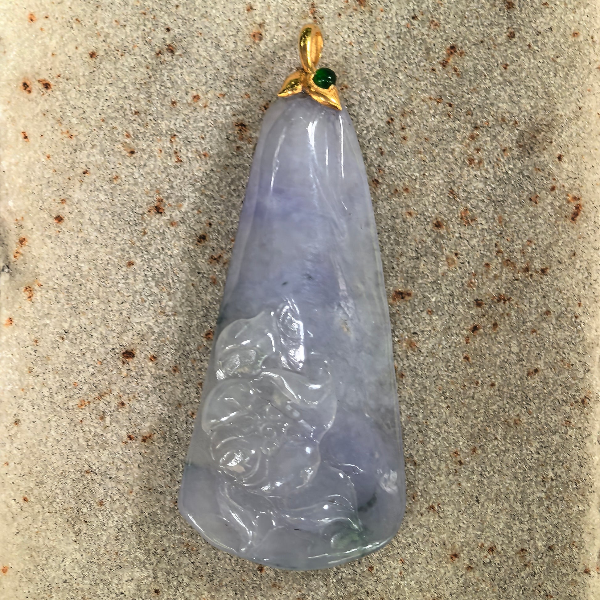 Close-up of icy glutinous blue-lavender lotus jadeite pendant on stone background with carved lower lotus detail.

