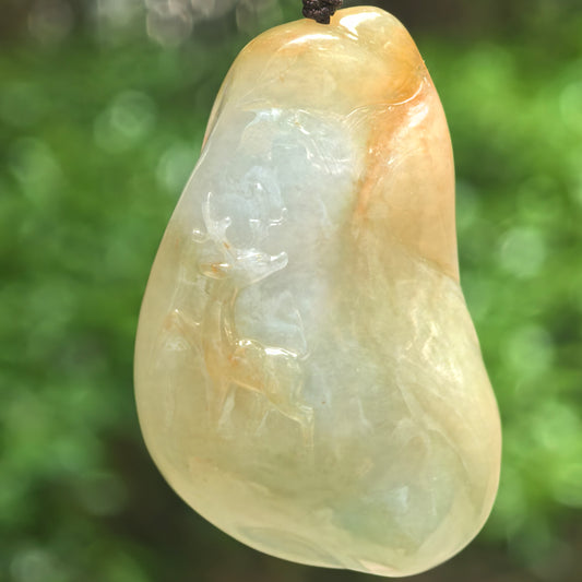 Close-up of glutinous yellow-green deer jadeite pendant hanging outdoors with carved deer motif.
