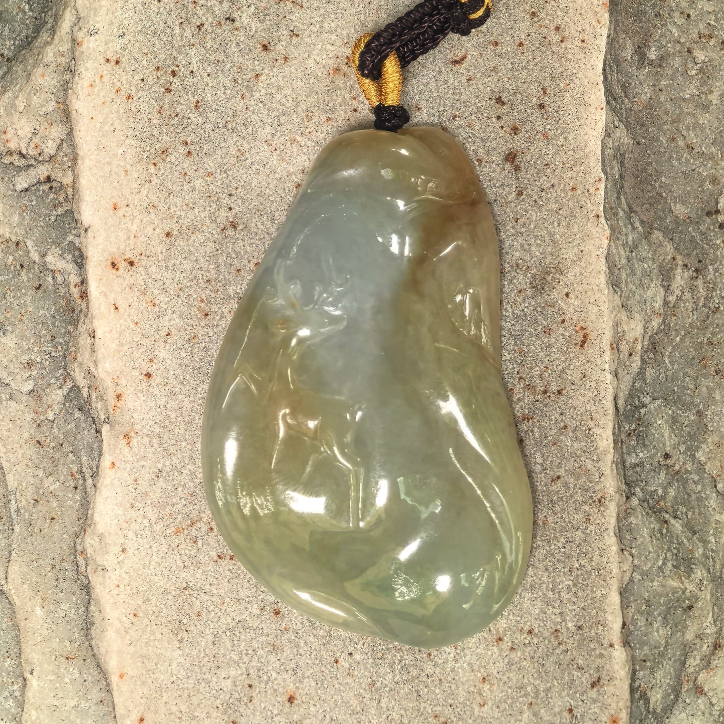 Natural Grade-A yellow-green deer jadeite pendant placed on stone background showing rounded thick carving.
