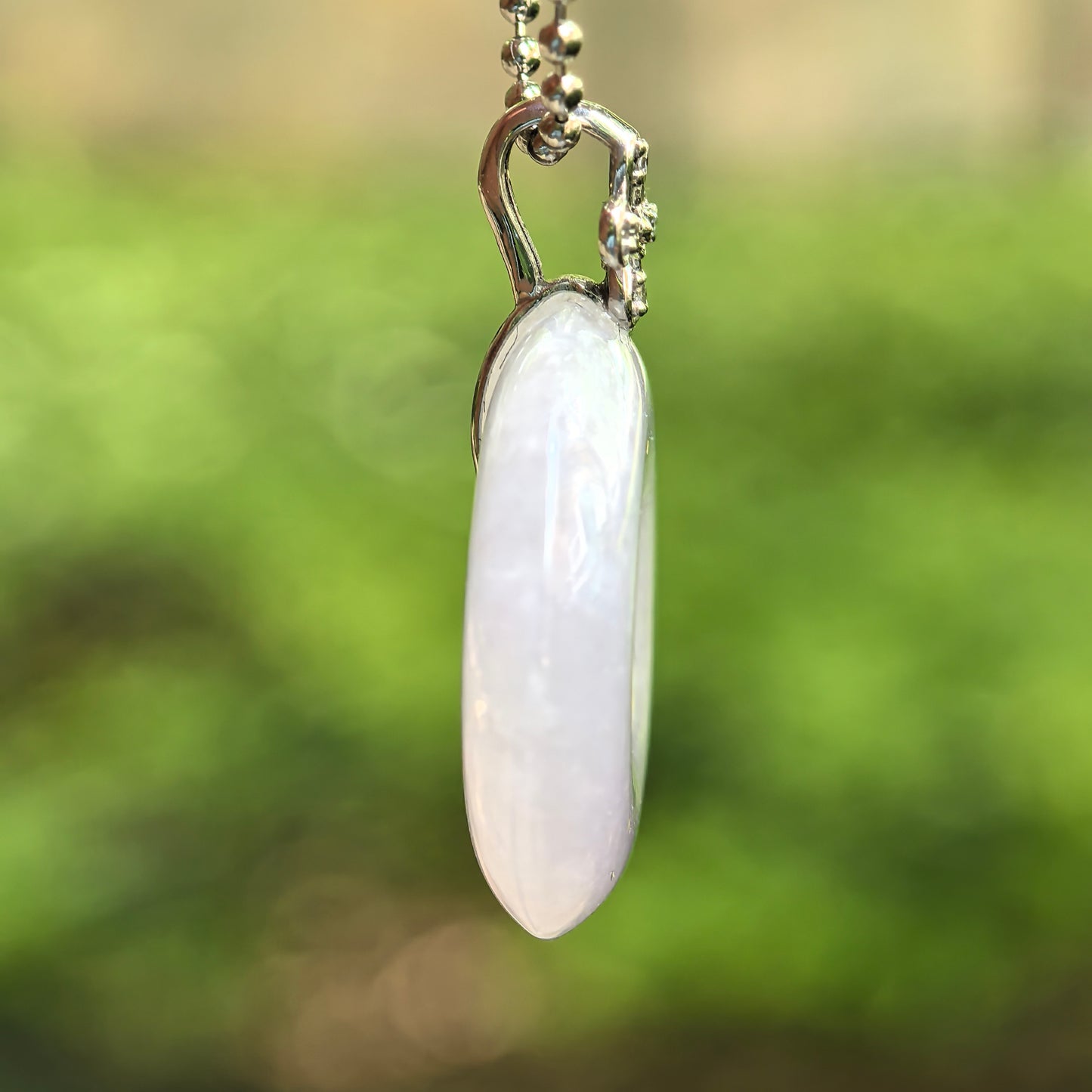 Side view of glutinous light lavender jadeite Peace Pendant showing rounded thickness and 18K gold bail.

