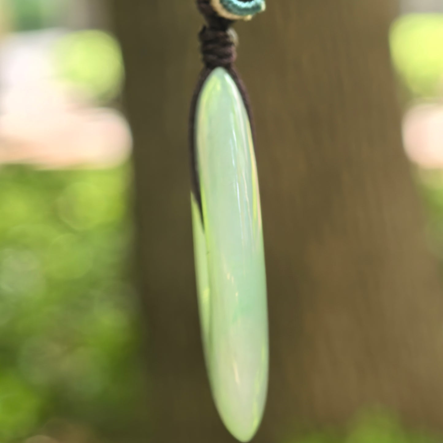 Side view of light green jadeite Peace Pendant showing its thick rounded profile and cord.
