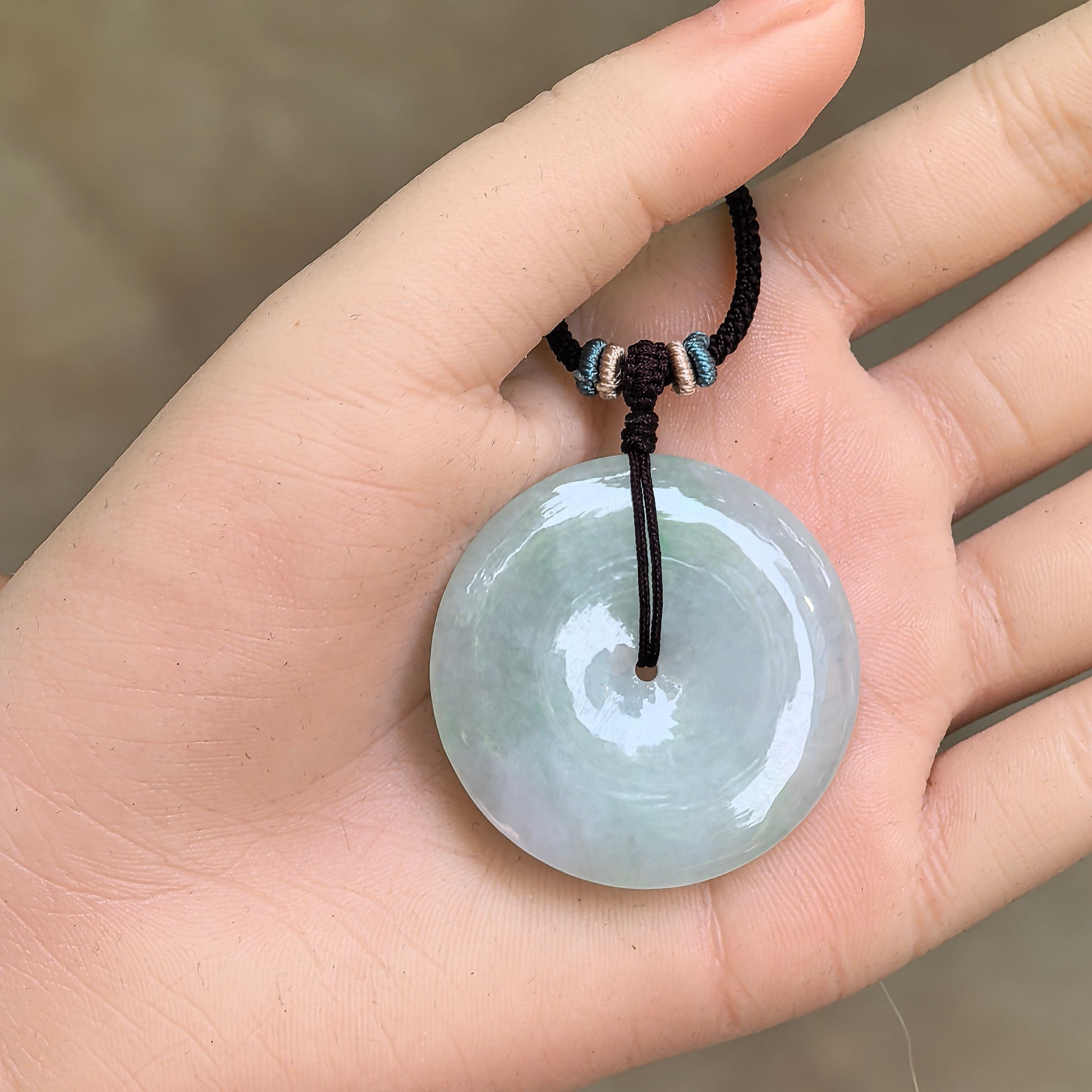Natural Grade-A light green jadeite Peace Pendant displayed in hand with cord included.
