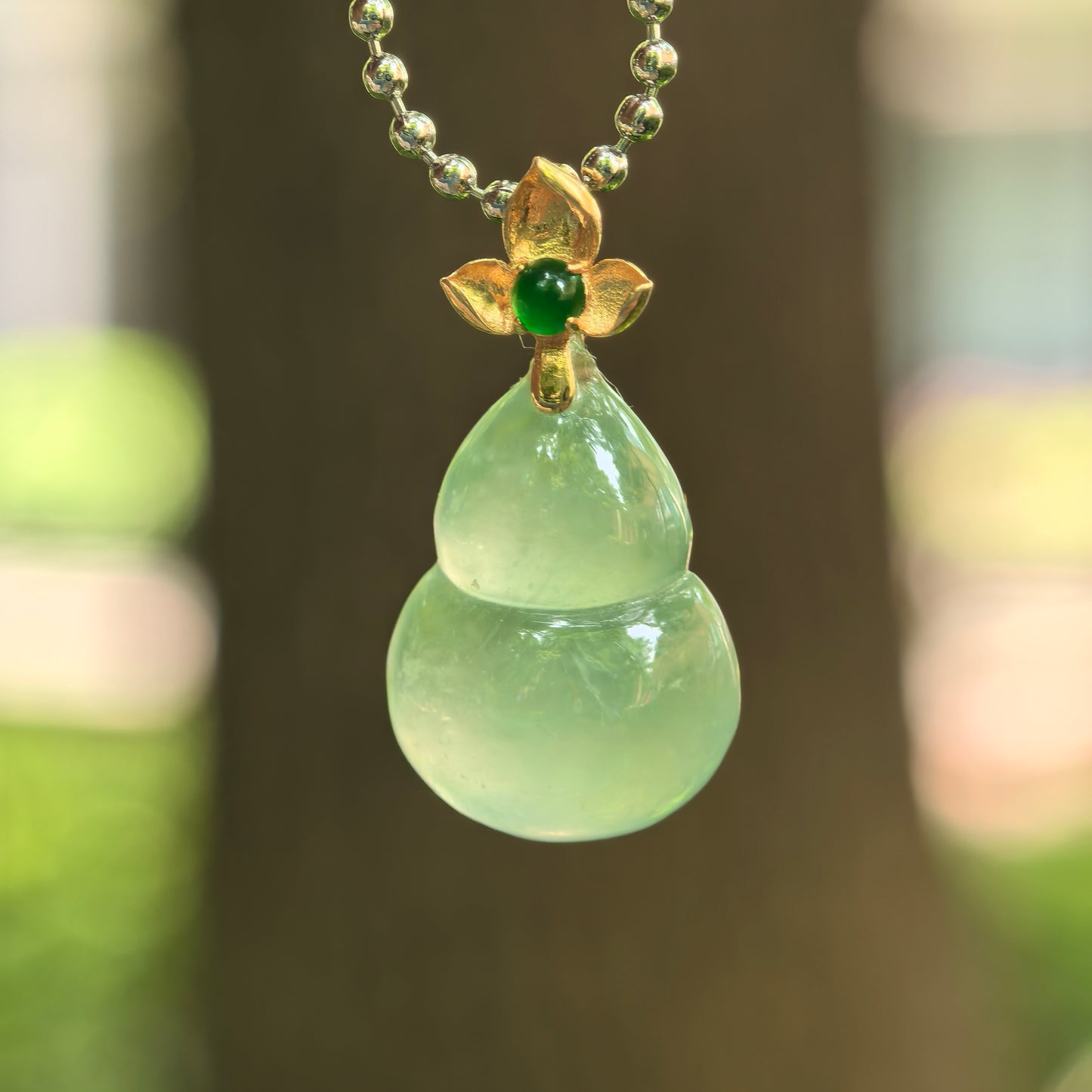 Natural Grade-A icy light green gourd jadeite pendant with 18K gold floral bail.
