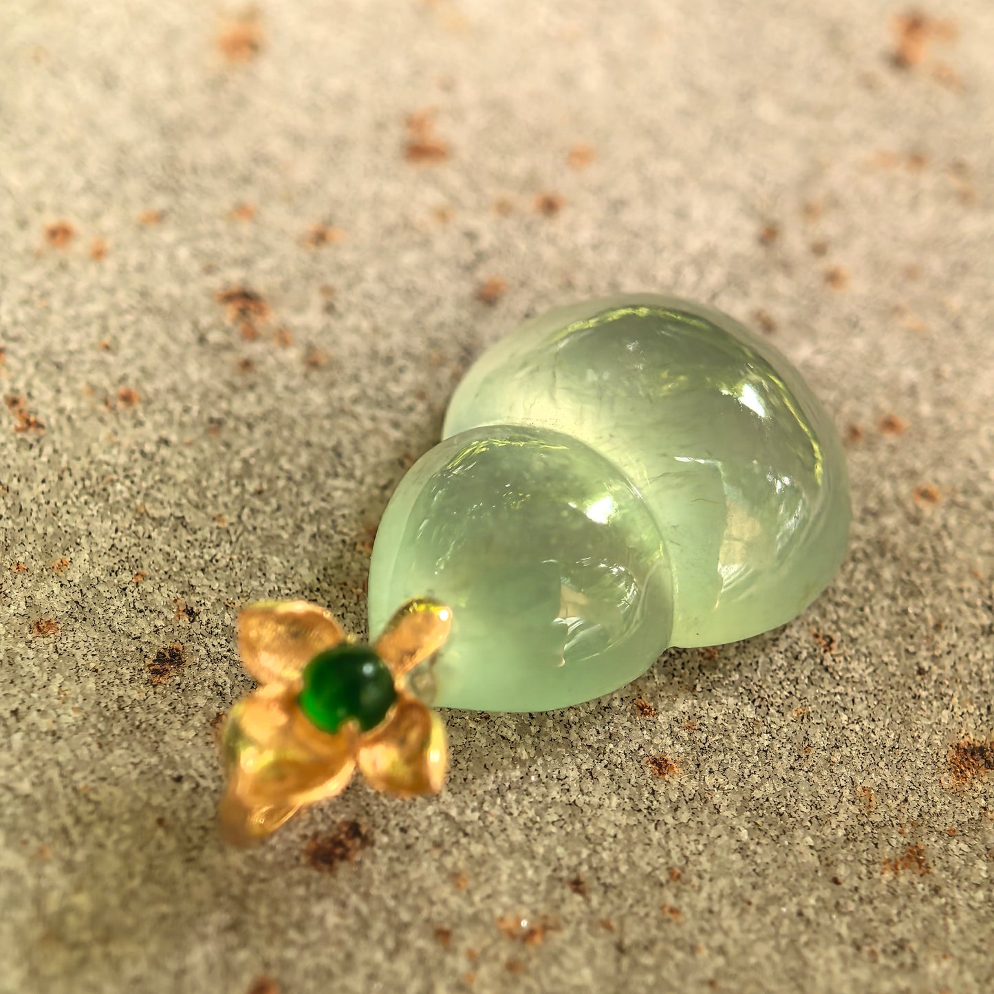 Icy light green jadeite gourd pendant placed on stone background.
