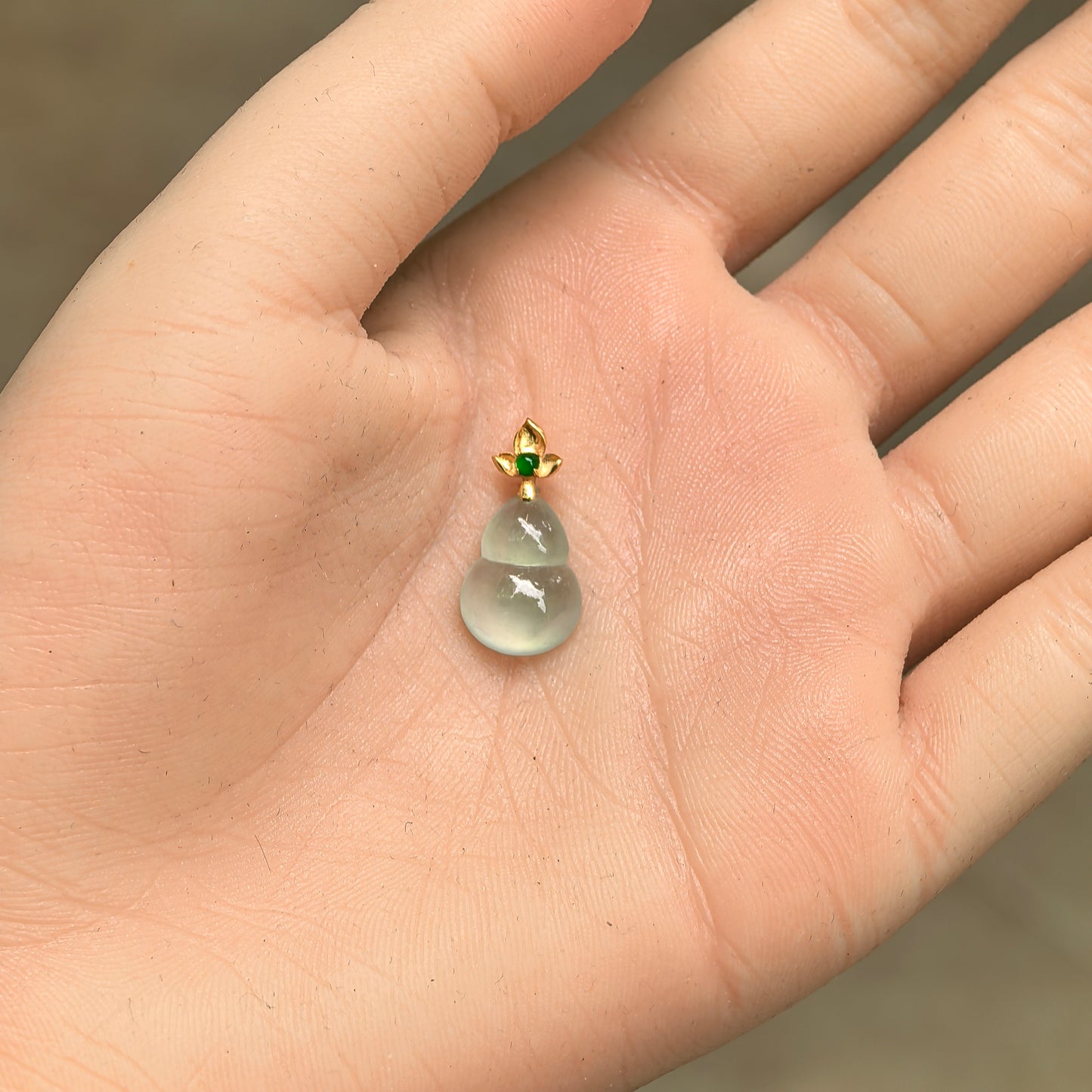 Petite 18K gold gourd jadeite pendant displayed in hand for size reference.
