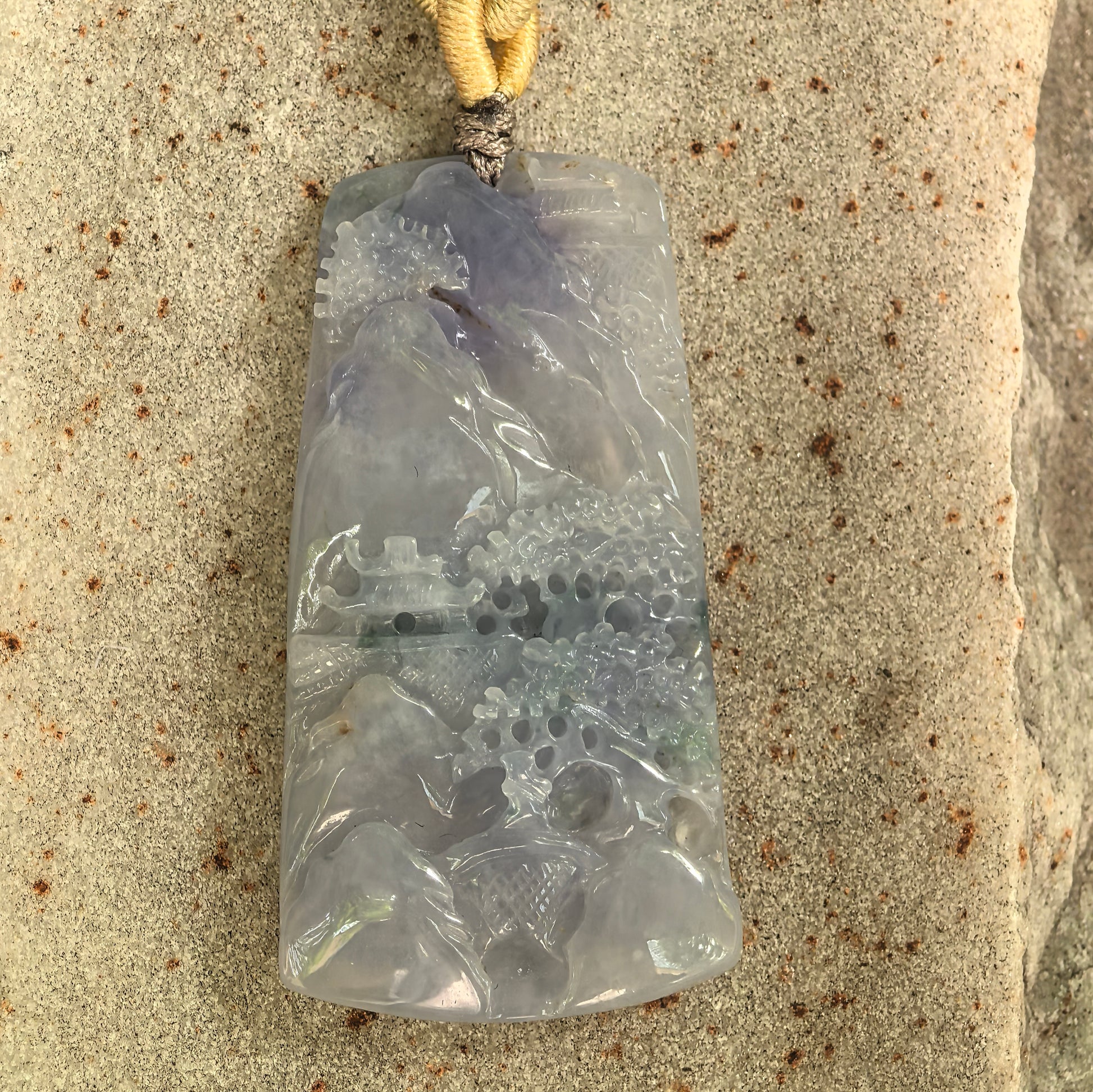 Close-up of purple landscape jadeite pendant showing carved mountain, pavilion, and floral details.

