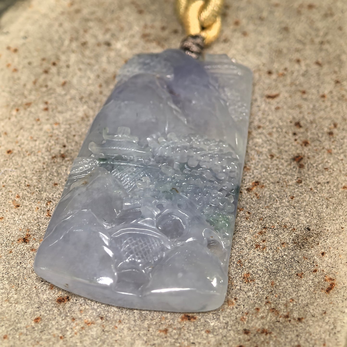 Icy glutinous purple jadeite landscape plaque pendant displayed on stone with soft translucency.
