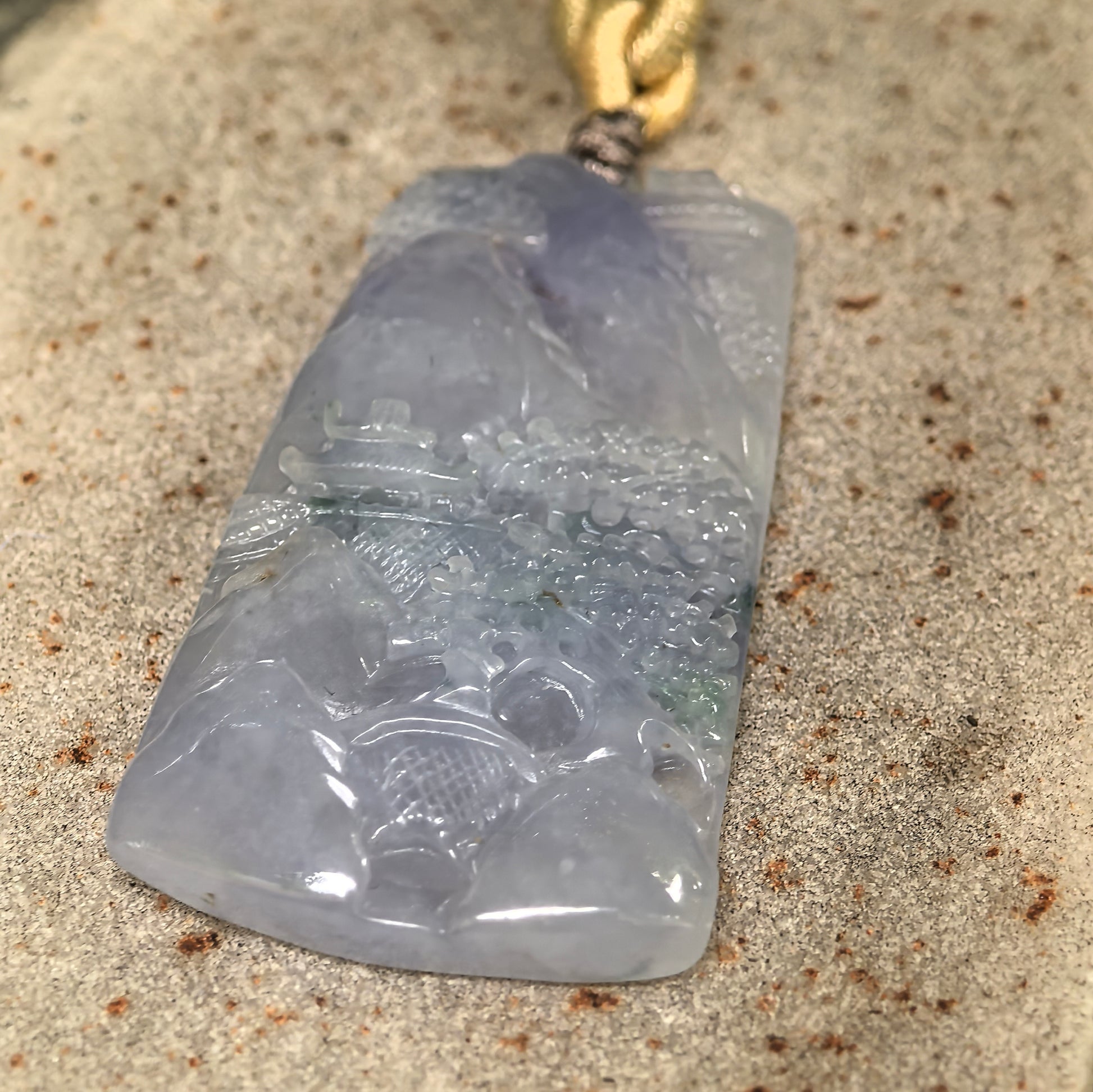 Icy glutinous purple jadeite landscape plaque pendant displayed on stone with soft translucency.
