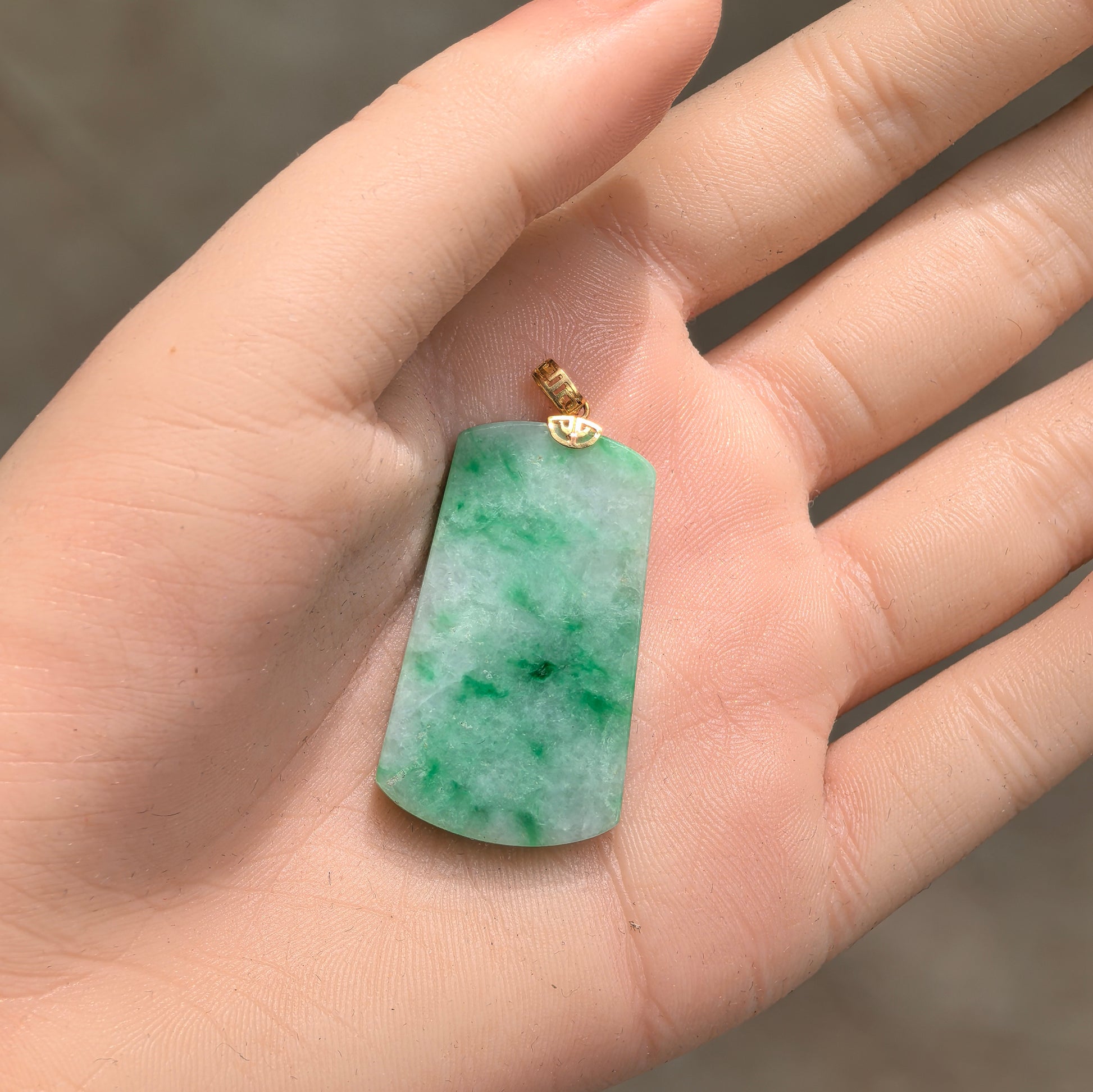 Light green jadeite plain plaque pendant shown in hand with compact trapezoid shape.

