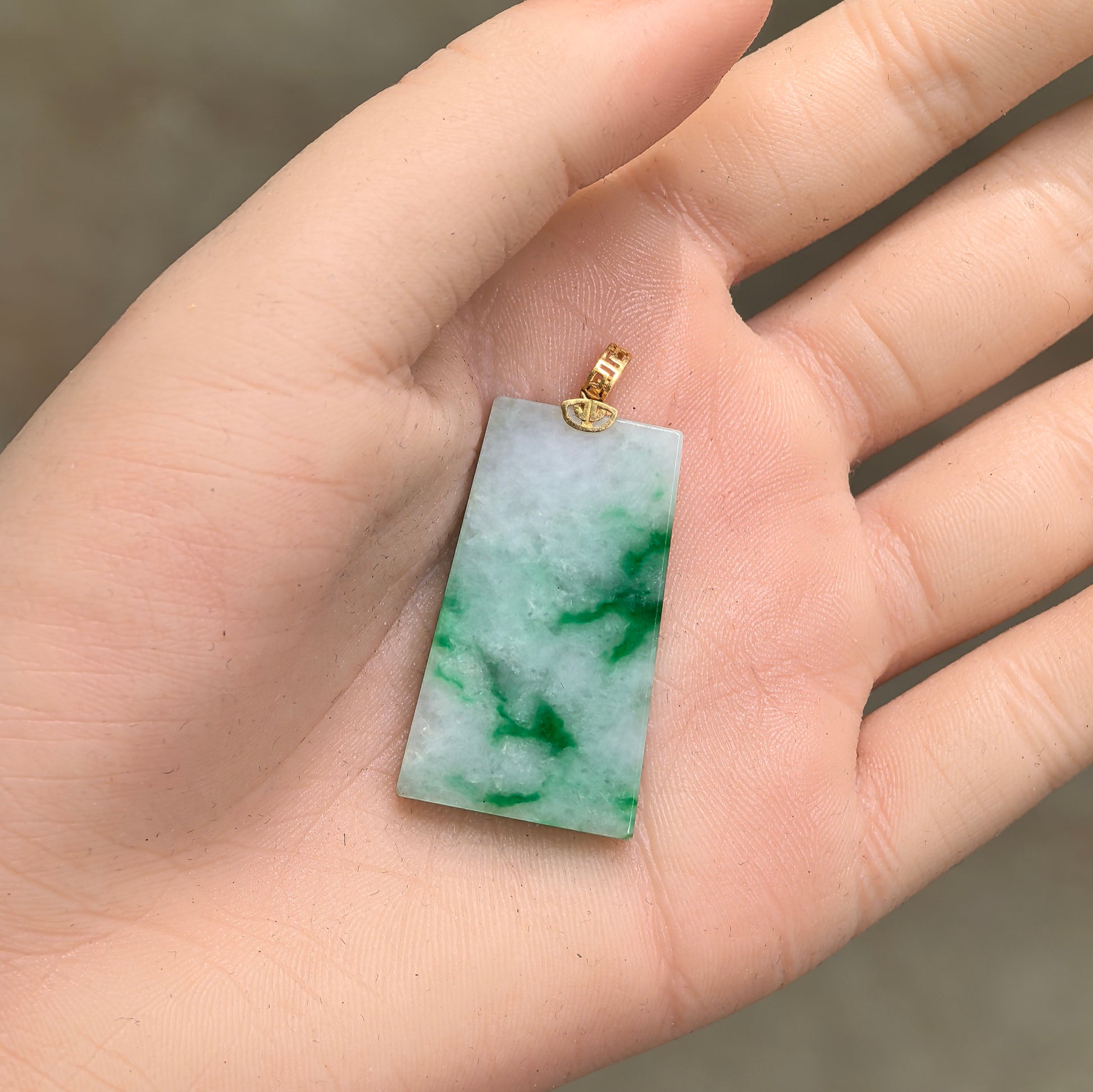 Light green jadeite plain plaque pendant shown in hand with natural floating green patterns.
