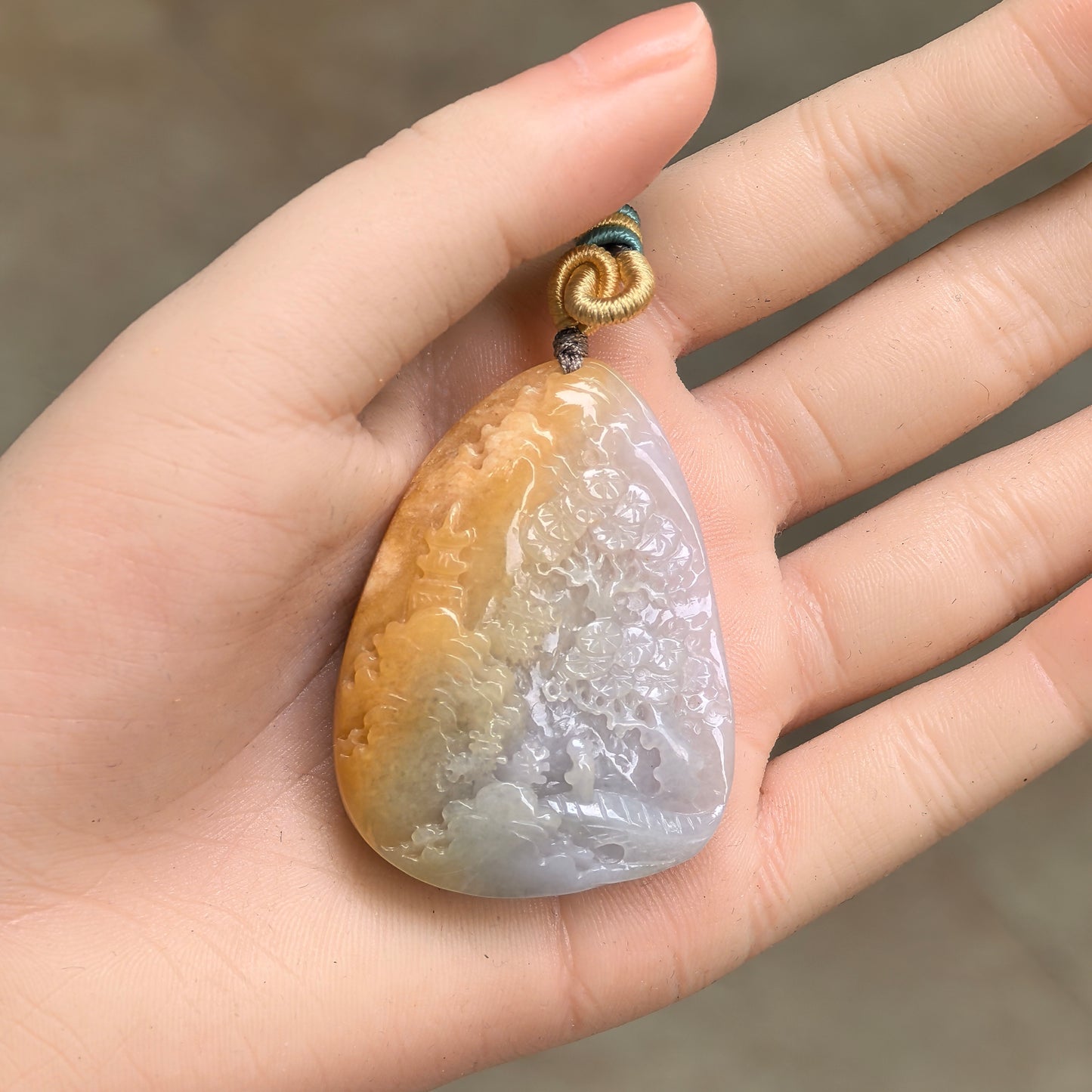 Large glutinous yellow-white landscape jadeite pendant shown in hand with carved scenery details.
