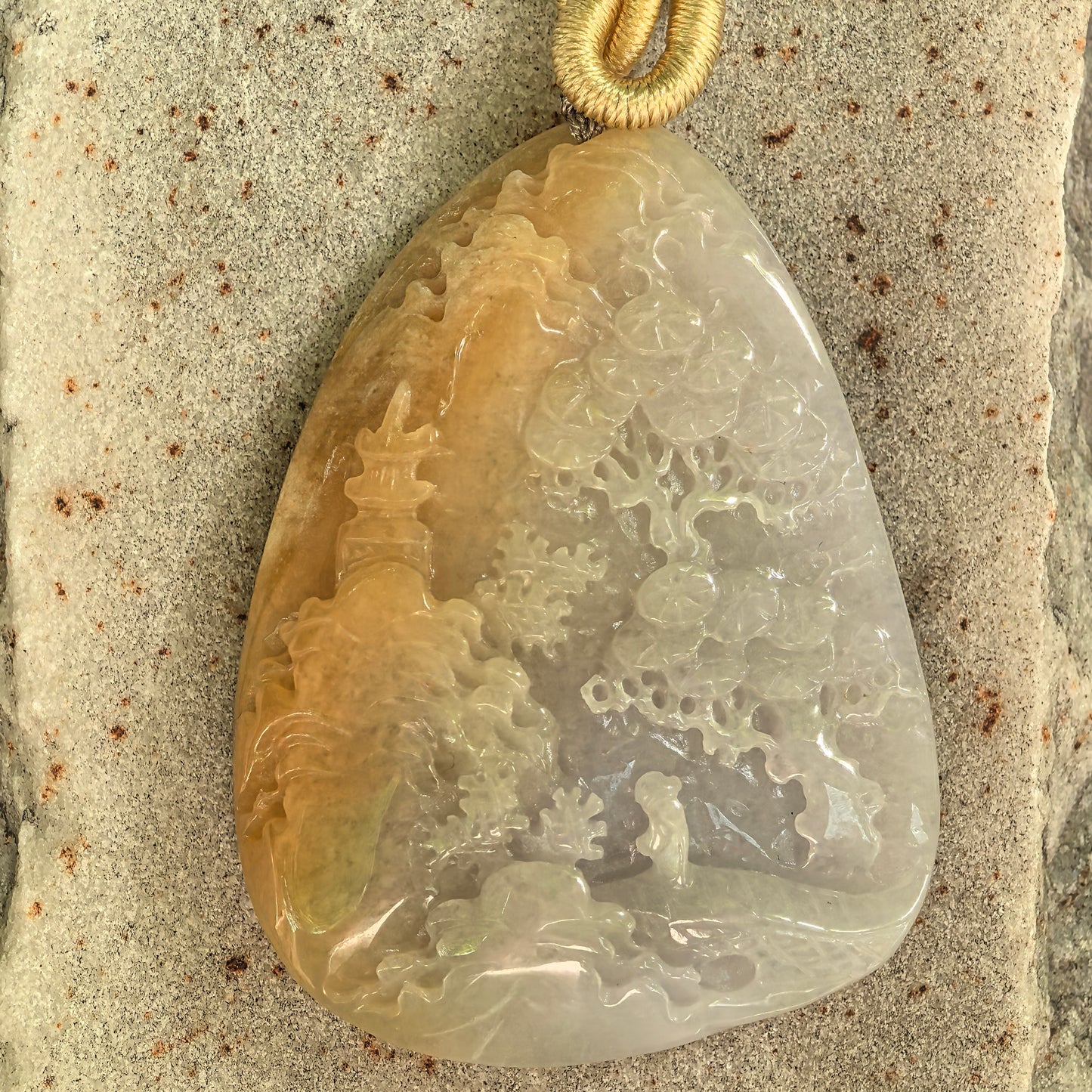 Close-up of honey-yellow and white landscape jadeite pendant showing pavilion and tree carving.
