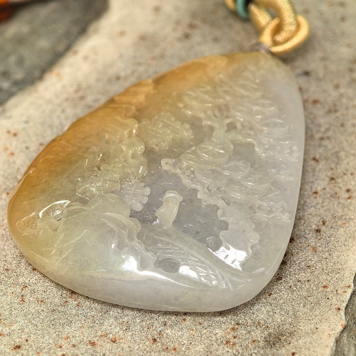 Macro view of carved landscape jadeite plaque pendant with smooth glutinous texture and natural color zoning.

