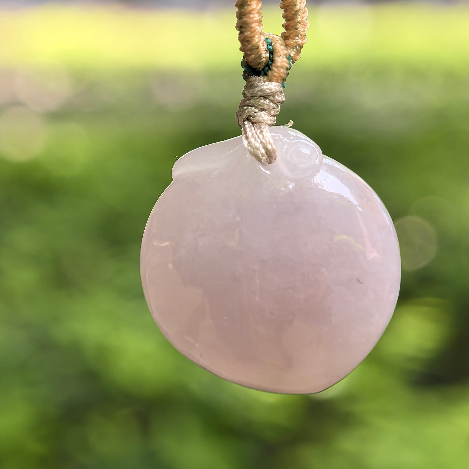 Natural Grade-A glutinous pink peach jadeite pendant hanging on woven cord under natural light.
