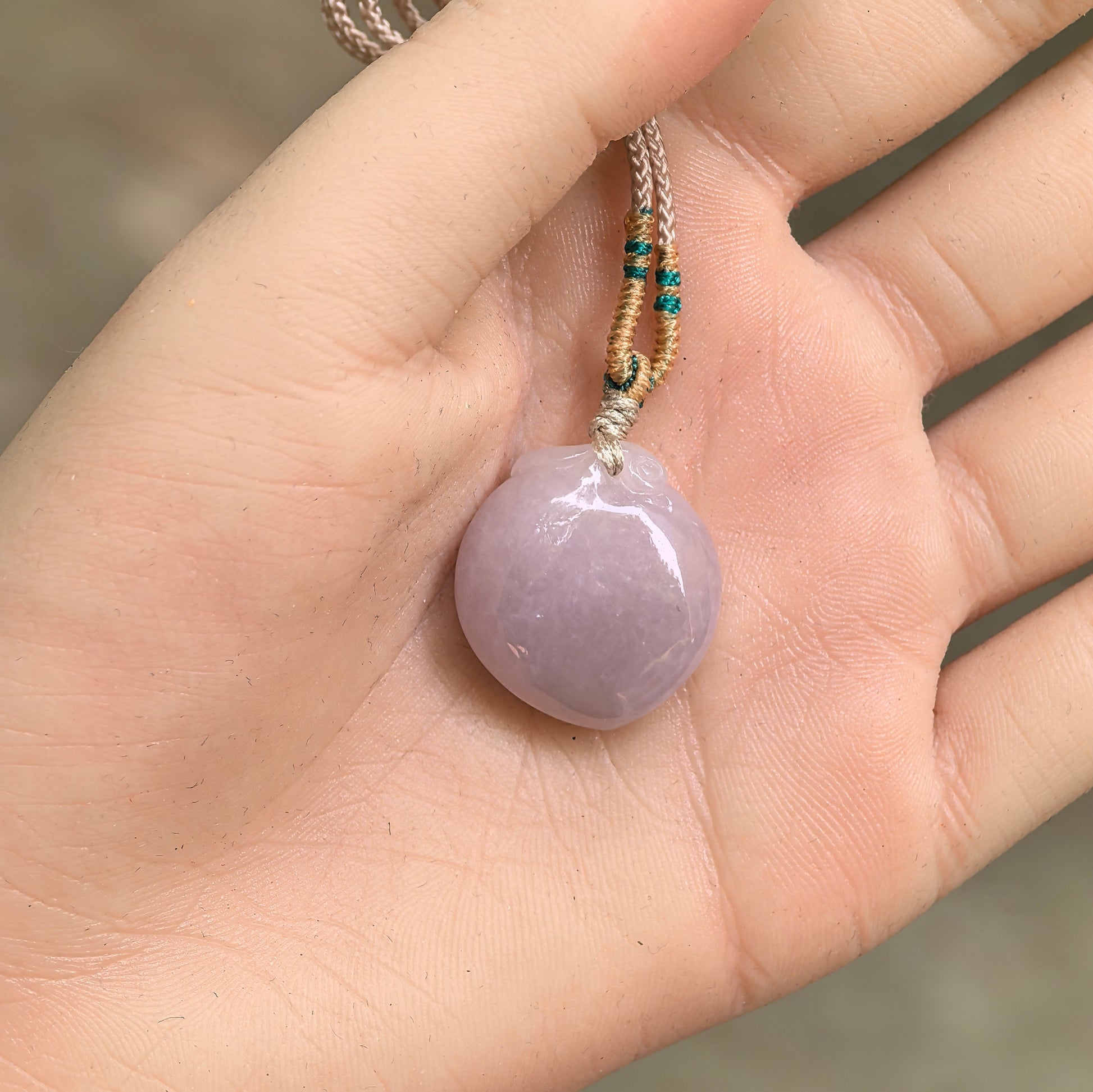 Soft pink peach jadeite pendant shown in hand with rounded carving and smooth luster.
