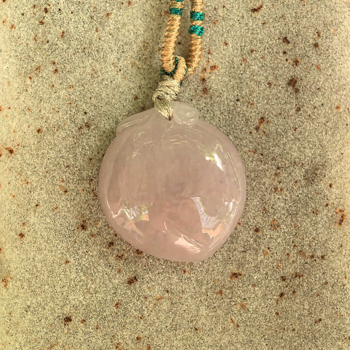 Close-up of glutinous pink jadeite peach pendant showing polished surface and soft texture.
