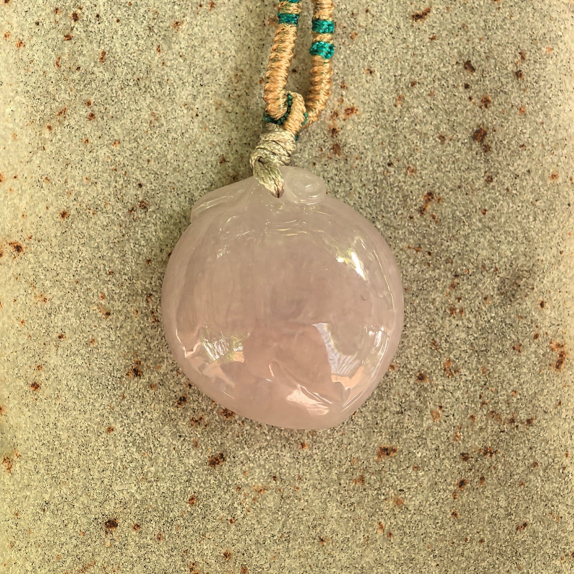 Close-up of glutinous pink jadeite peach pendant showing polished surface and soft texture.
