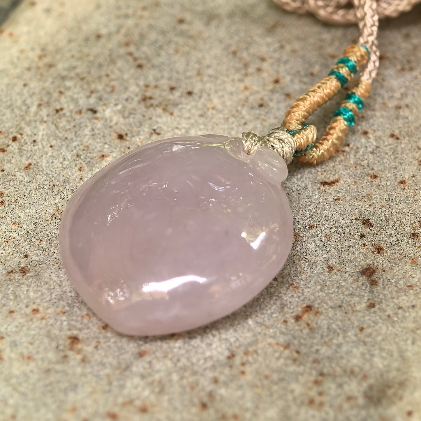 Side view of pink peach jadeite pendant with woven cord and rounded thickness.
