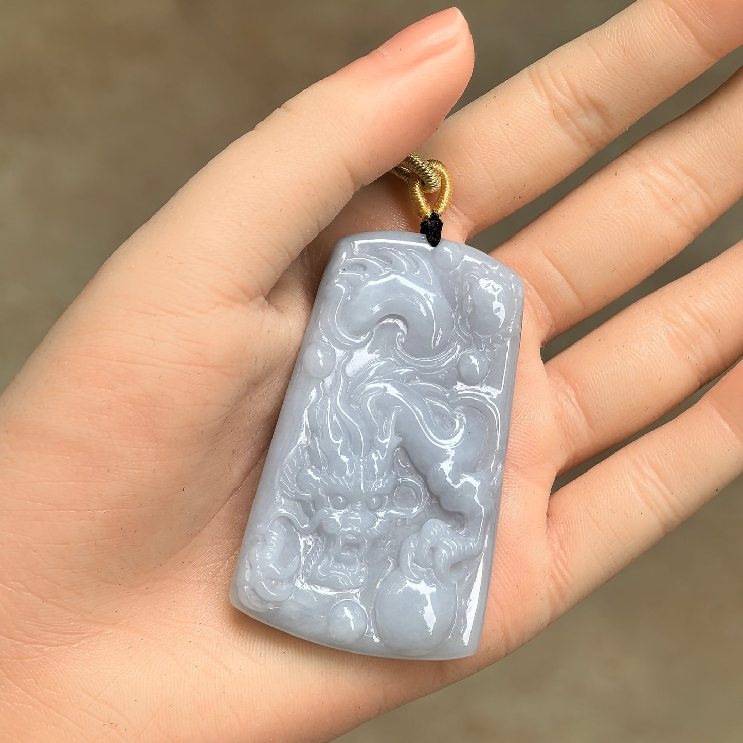 Blue base dragon jadeite plaque pendant shown in hand with cord and glossy surface luster.
