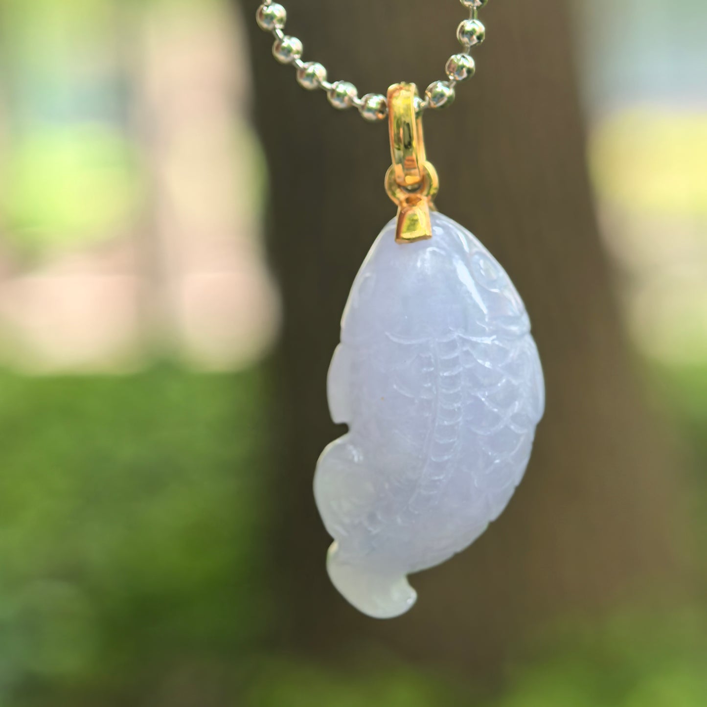 Close-up of lavender fish jadeite pendant showing three-dimensional carving and polished texture.
