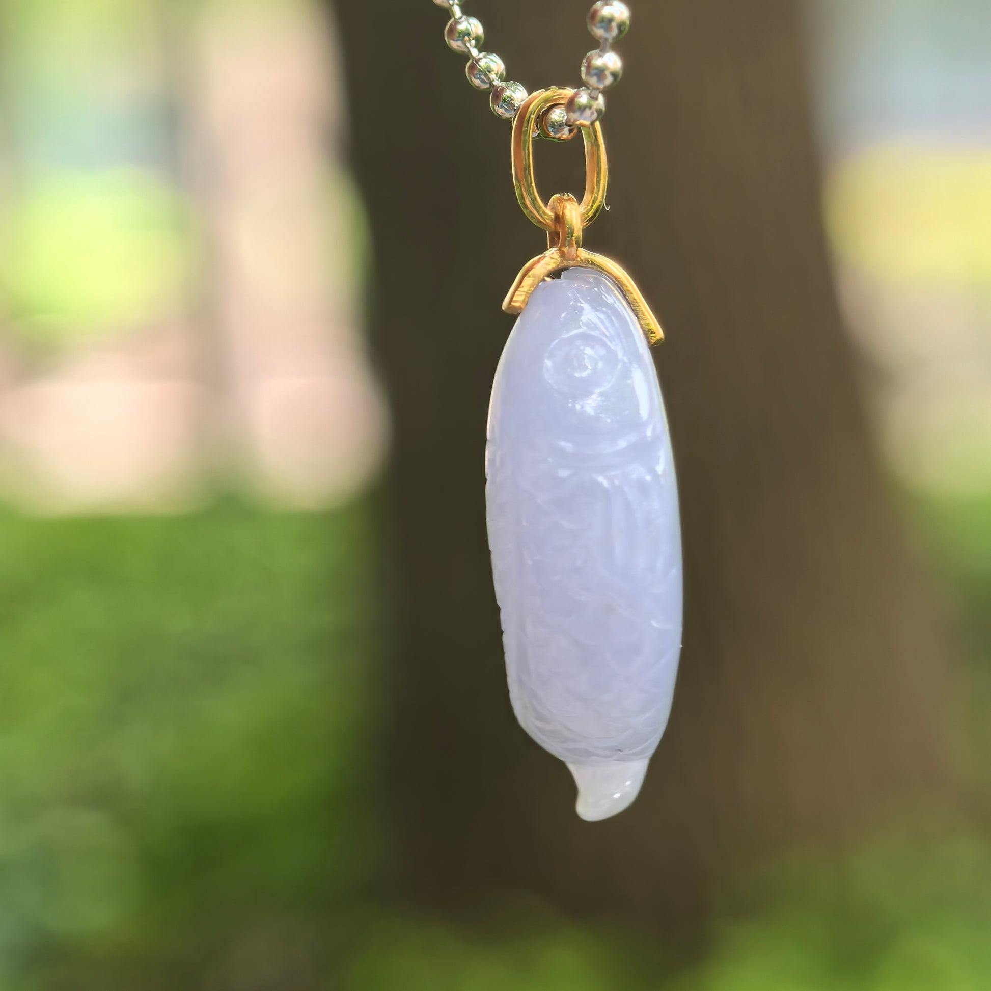 Side view of glutinous lavender jadeite fish pendant with detailed scale and tail carving.
